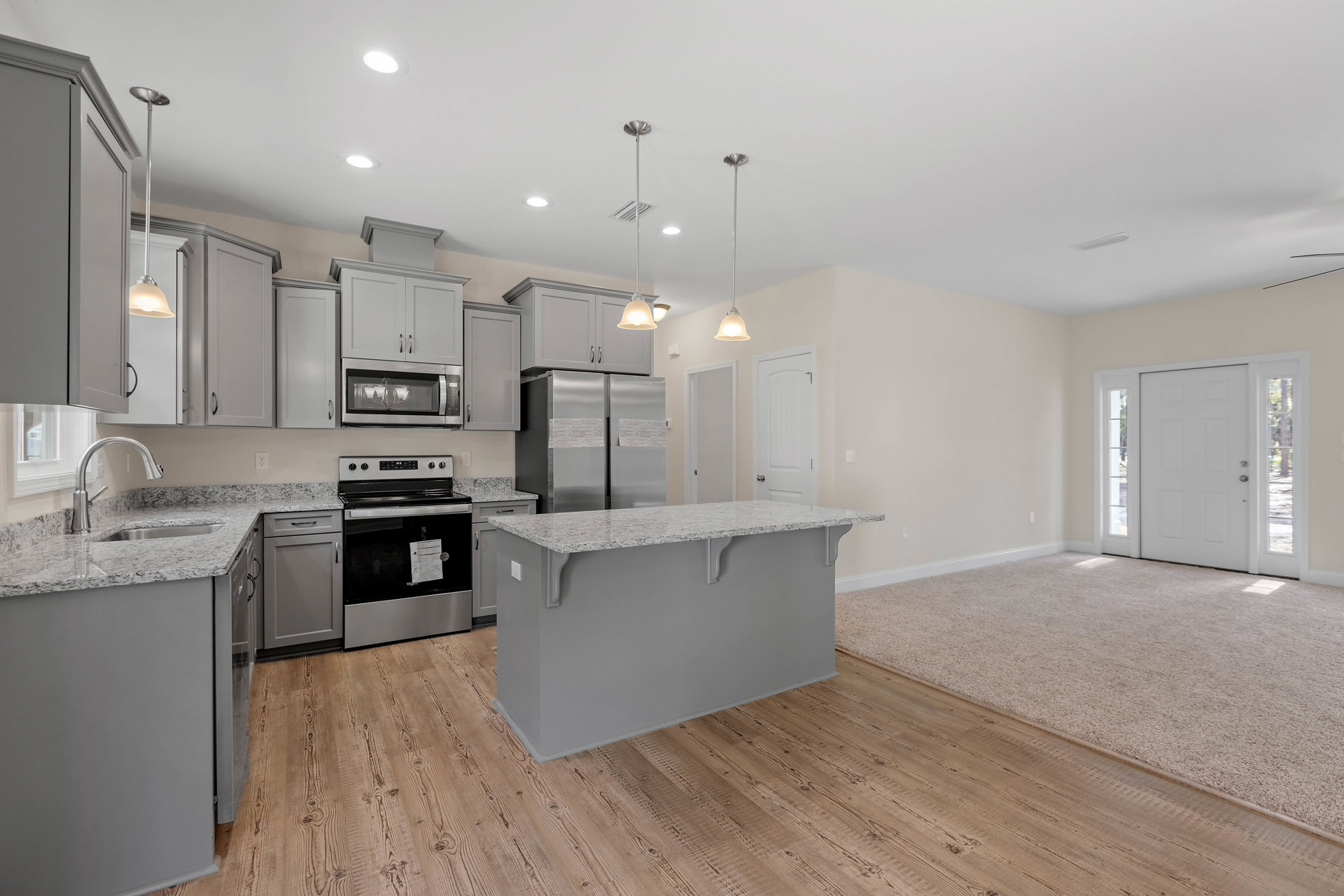 Spacious kitchen featuring a large central island, carpeted flooring, tiled backsplash, white cabinetry, stainless steel appliances including an oven with a paper attached to its