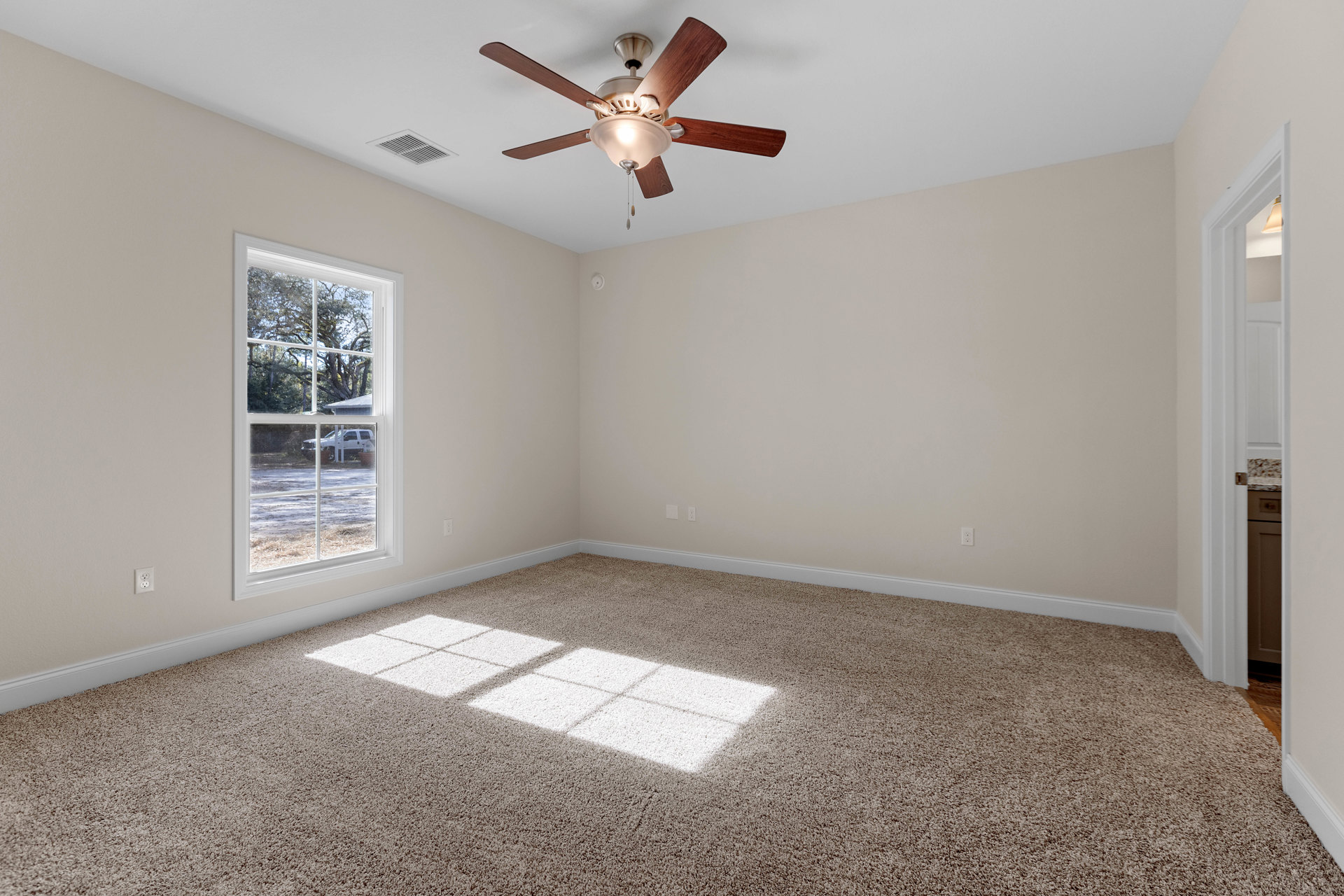 Carpeted room with a ceiling fan and light fixture, white-framed window overlooking a parked white truck, grey carpet with a white square, plaster walls and ceiling.
