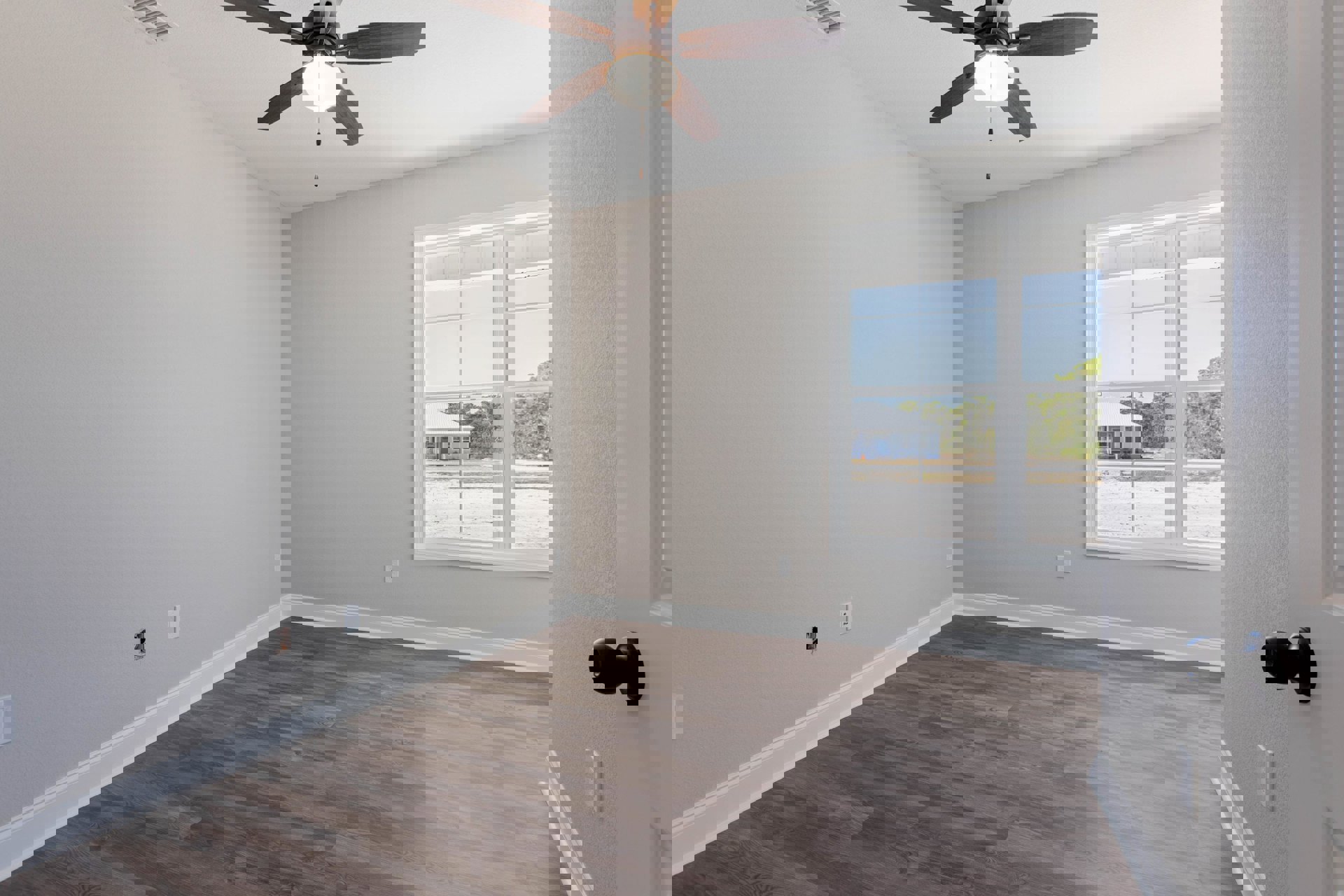 Ceiling fan with light fixture mounted above wood flooring and white trim, window showing neighboring house, black wall-mounted object, blue front door visible outside