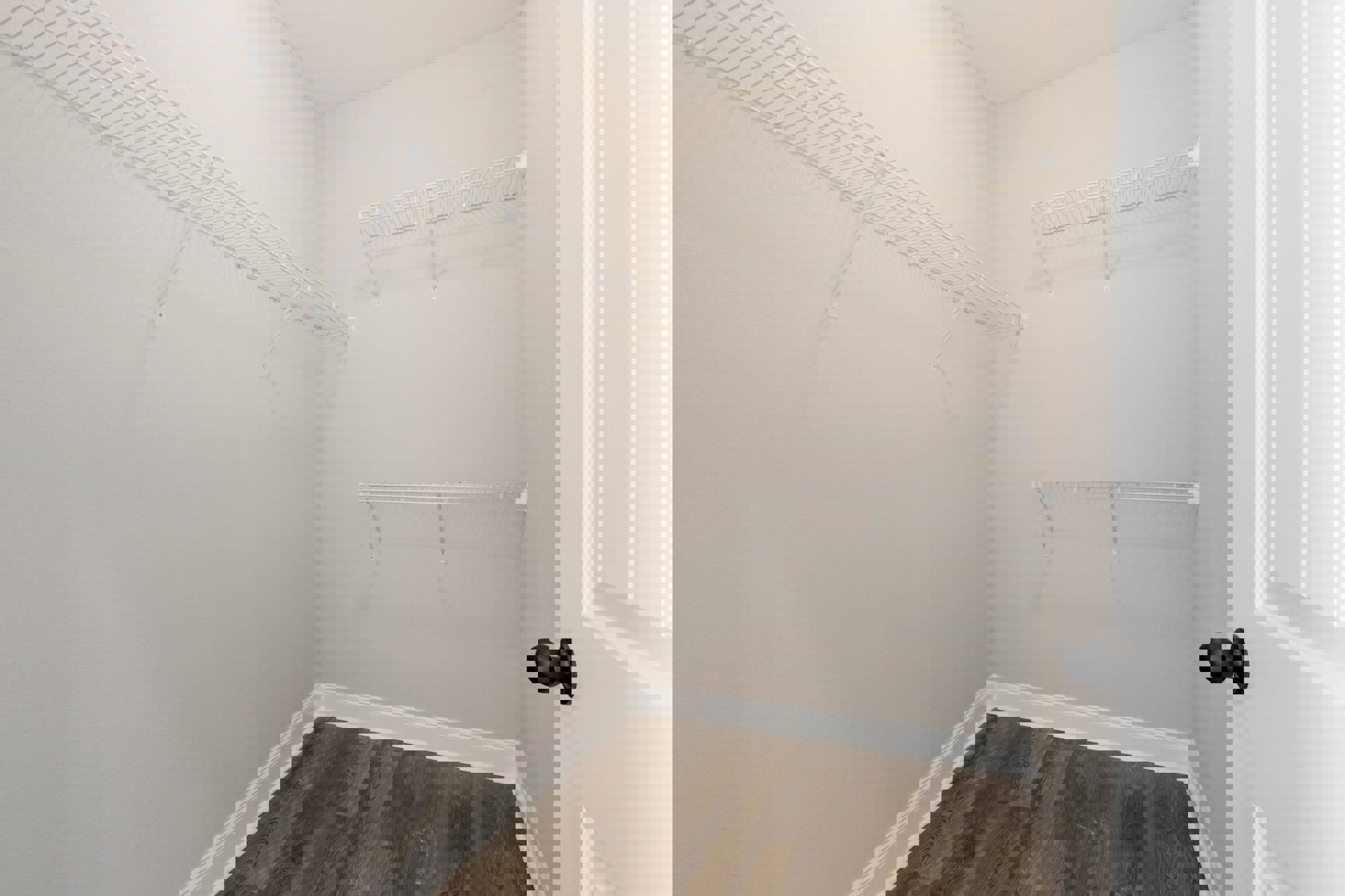 White closet with built-in shelves, wood flooring, white baseboards, and a white door featuring a black knob.