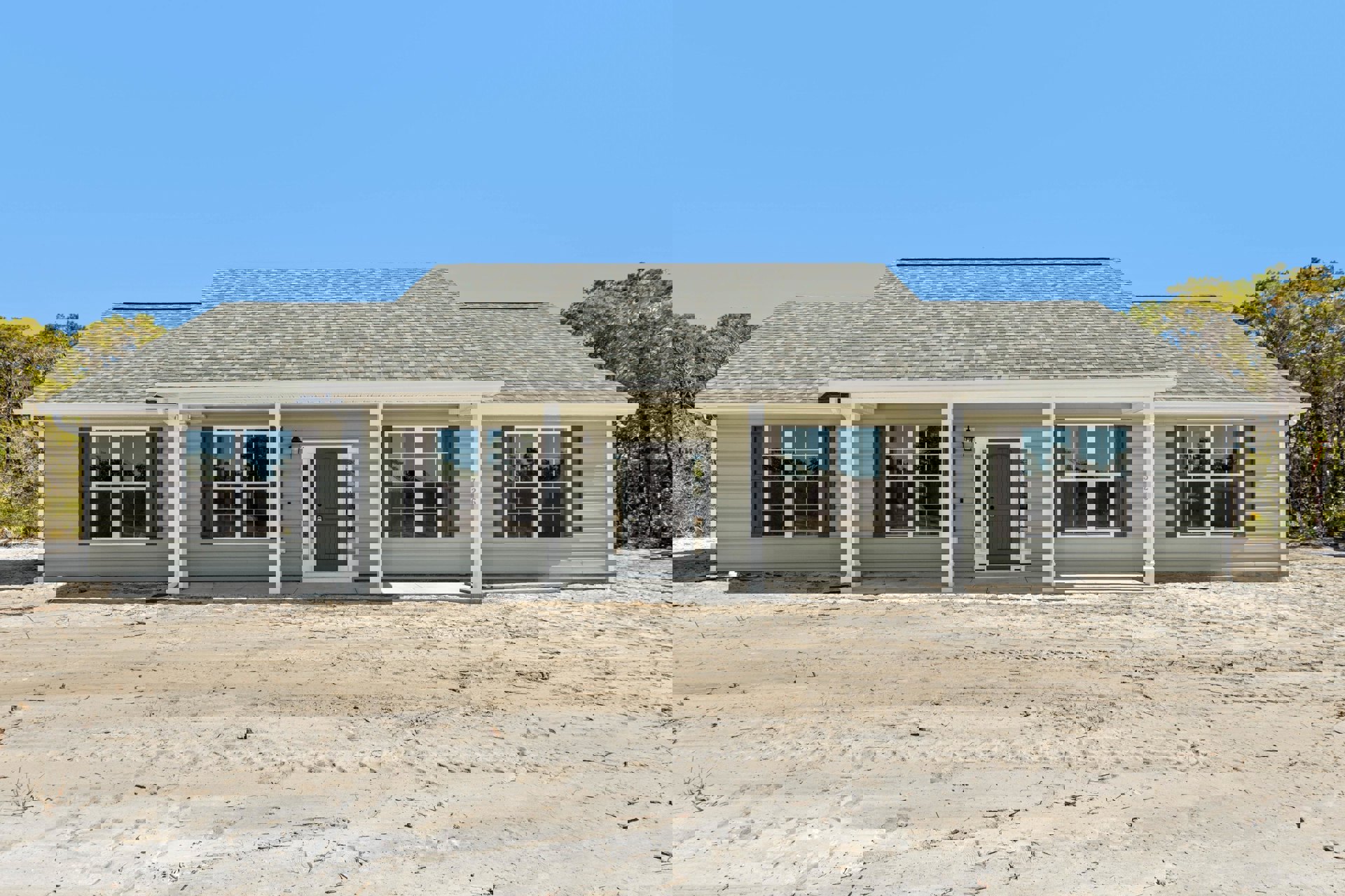 Two-story house with light siding, grey door with glass panes, multiple windows, dirt area and tire tracks in front, blue sky above