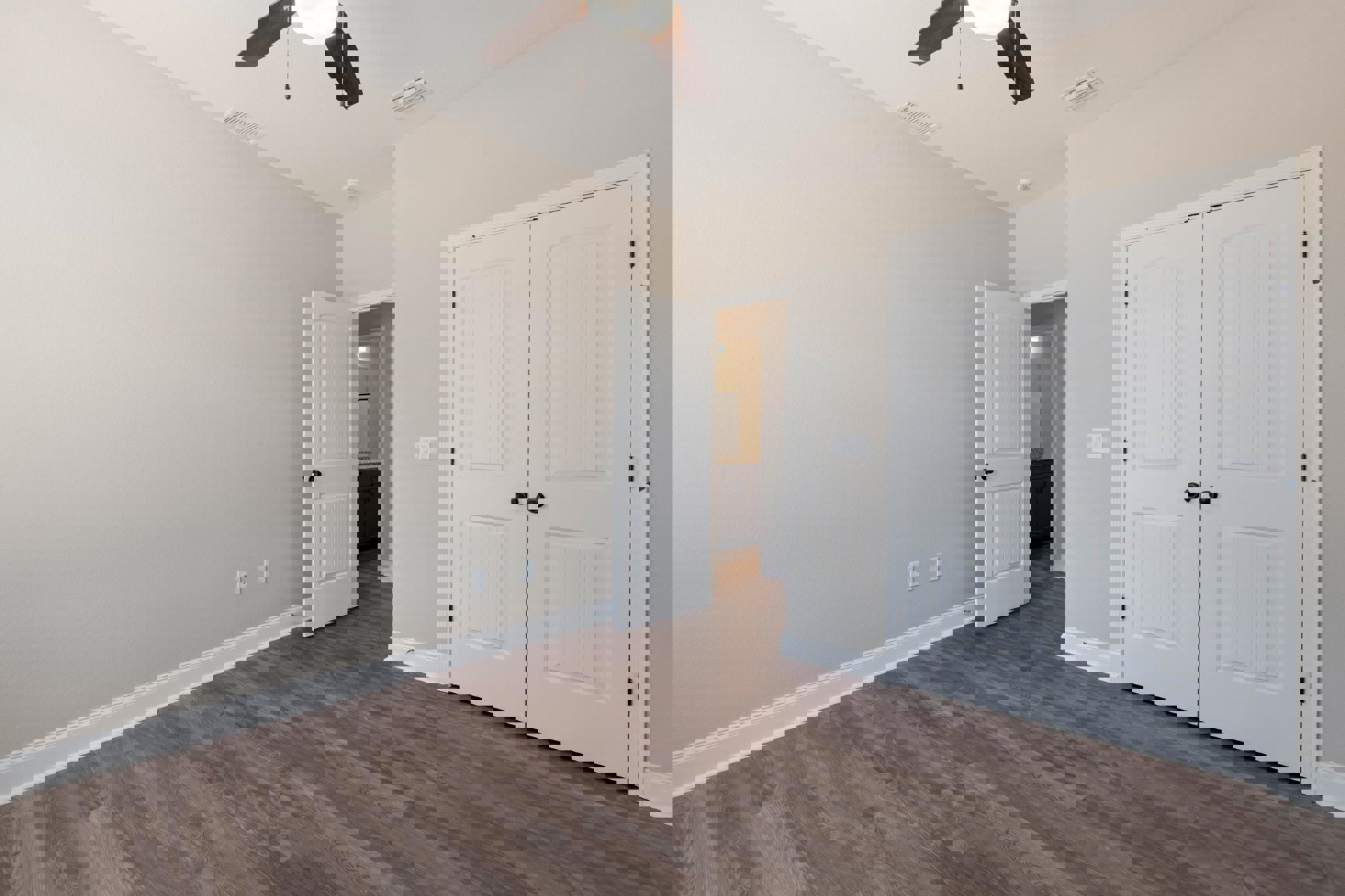 Room with wood flooring, white double doors with black knobs, white walls, and a ceiling fan with light fixture.