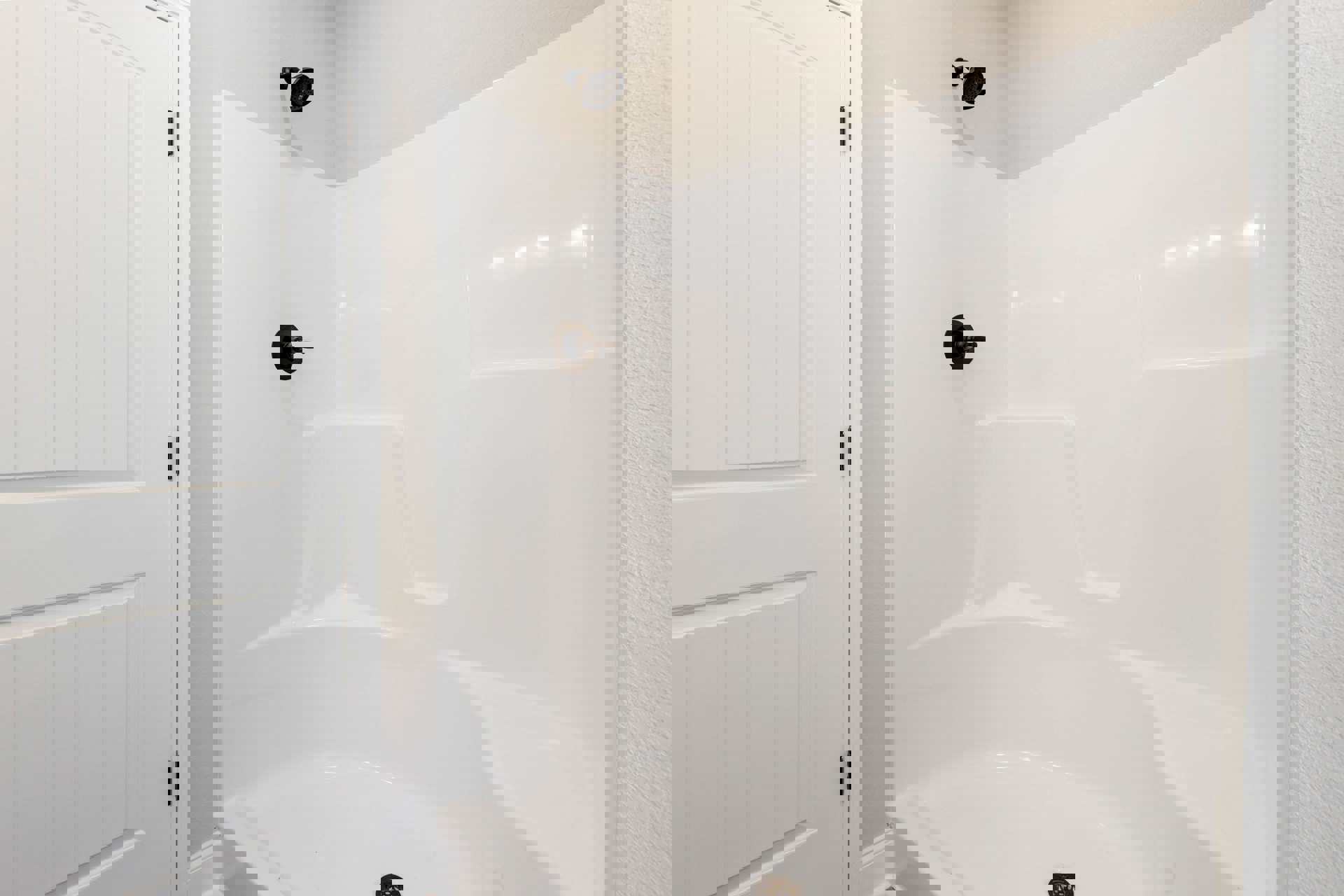 White tile shower with round chrome shower head, built-in drain, and white door featuring black hinge.