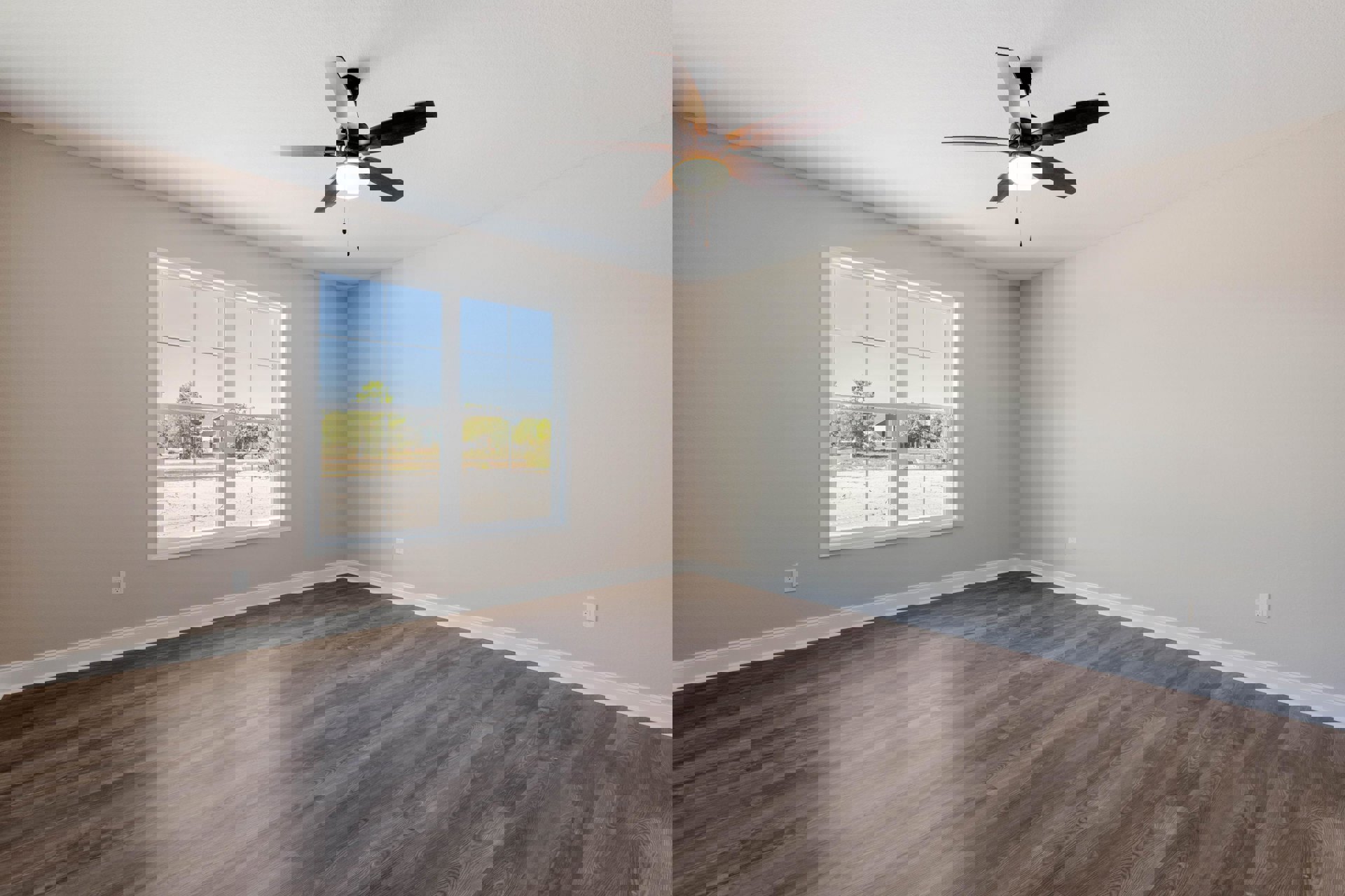 Ceiling fan with integrated light fixture, large window overlooking dirt road and trees, wood flooring with glossy finish reflecting light, white plaster walls
