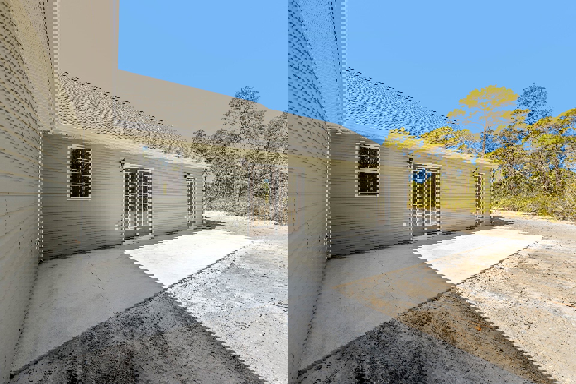 Two-story house with light-colored siding, white-framed windows, glass-paneled front door, paved driveway, and landscaped yard with trees.