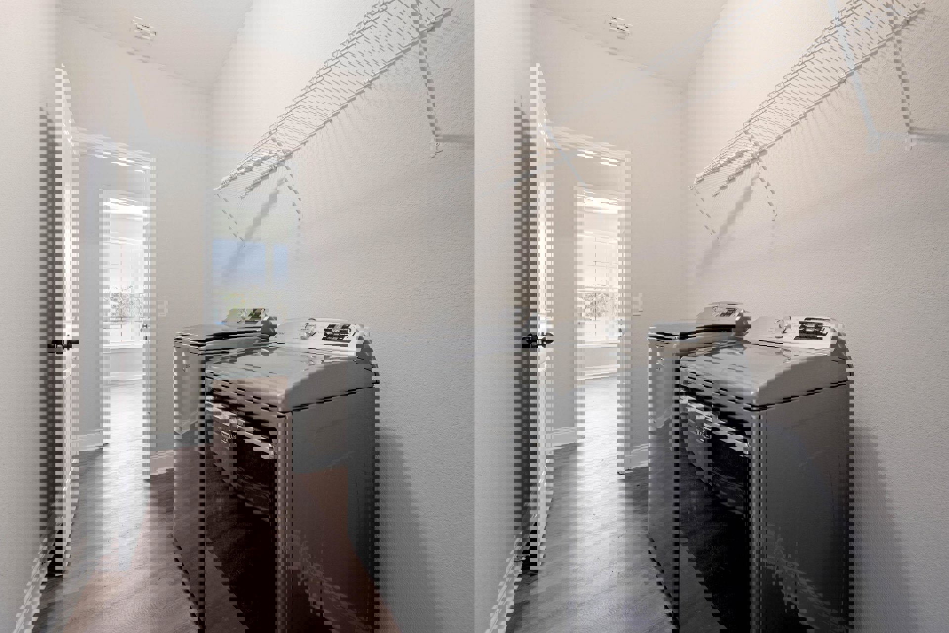 Laundry room with front-loading washer and dryer, white wire rack mounted on wall, open door, window showing neighboring house, light-colored cabinetry and flooring