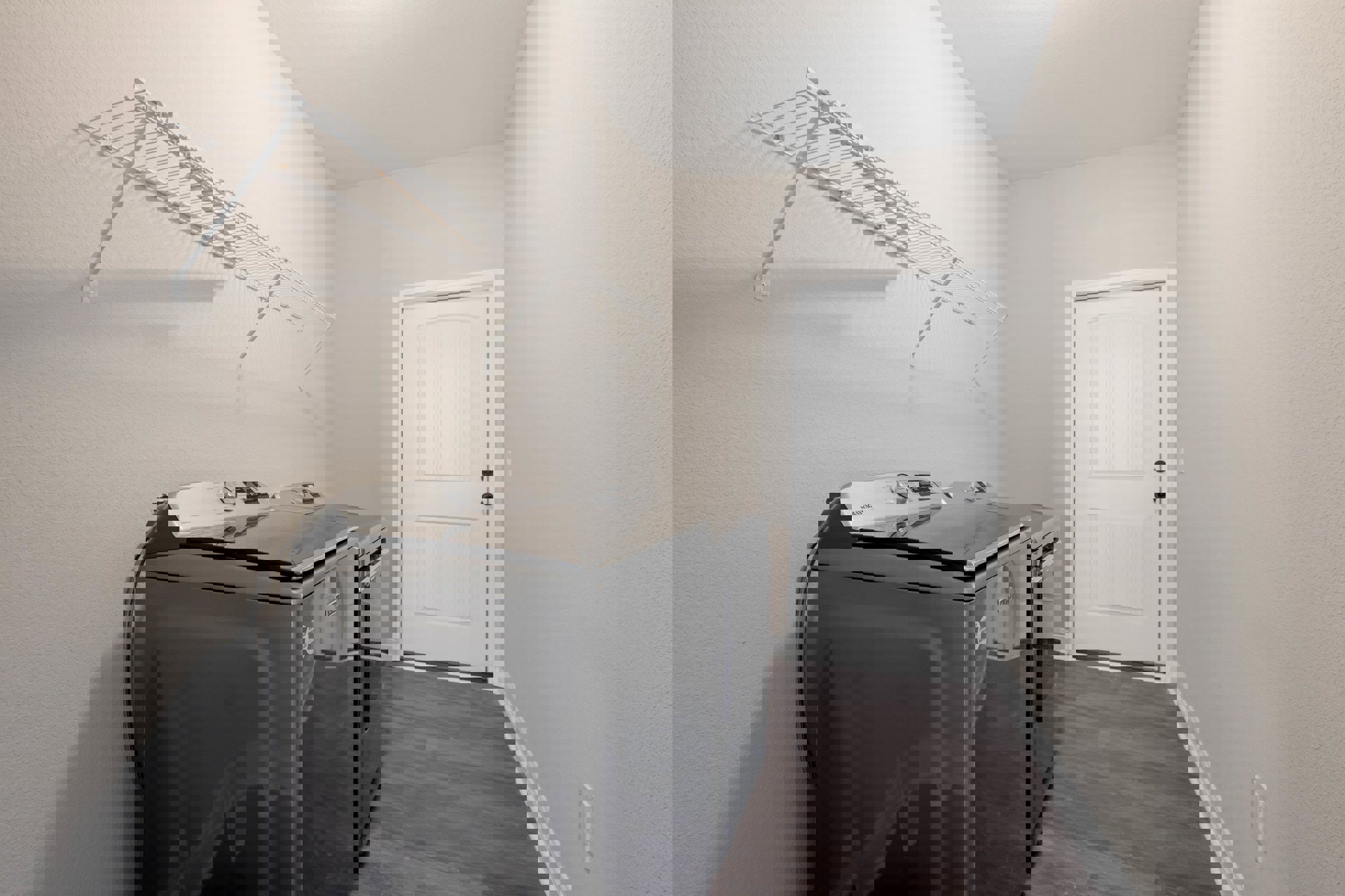 Laundry room with black washer and dryer, white shelving above, white door with black hardware, light-colored walls and ceiling, hard flooring