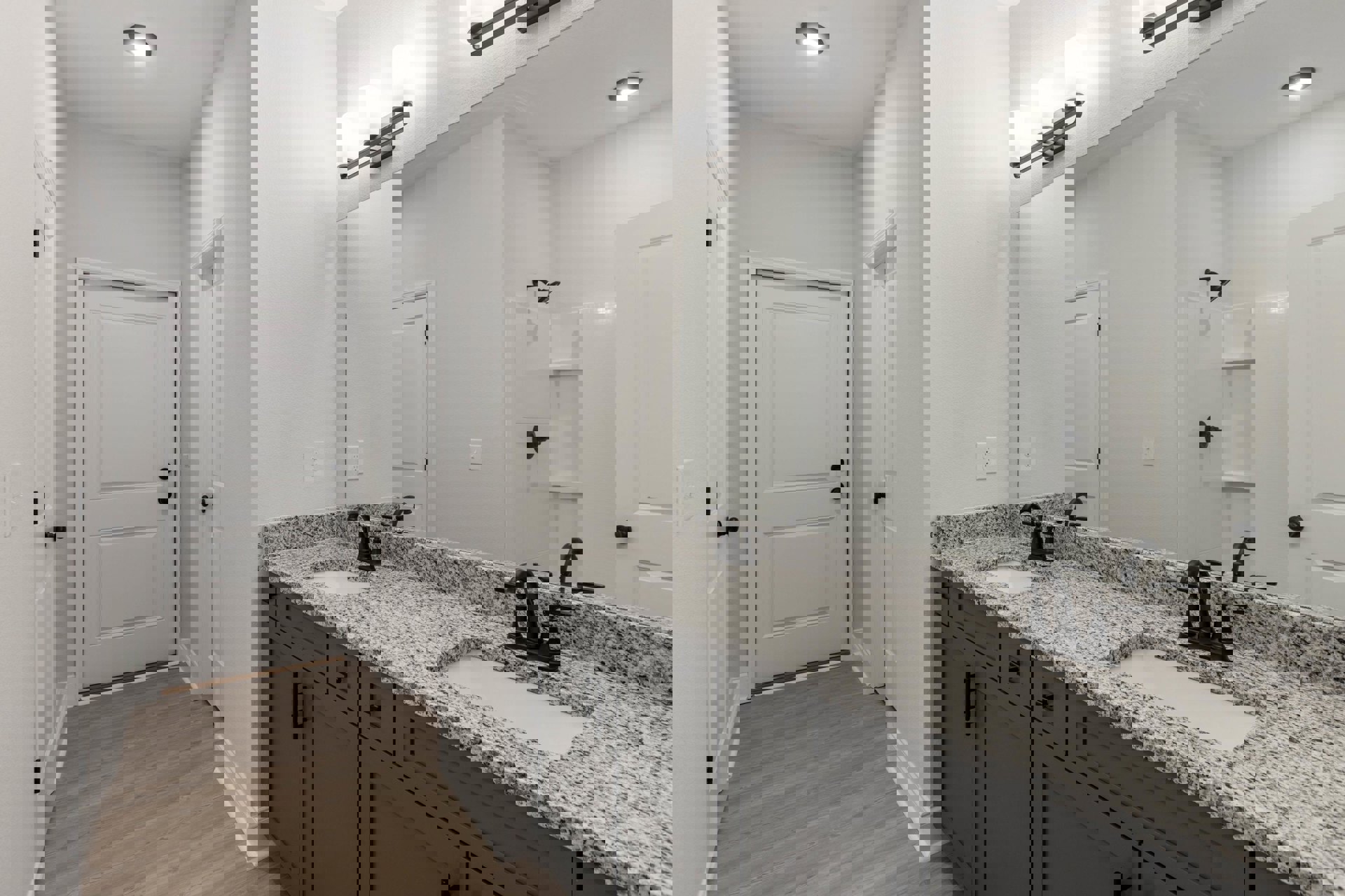 Bathroom with double vanity featuring black faucets, large wall mirror, wood flooring, white cabinetry, and white door with black hardware