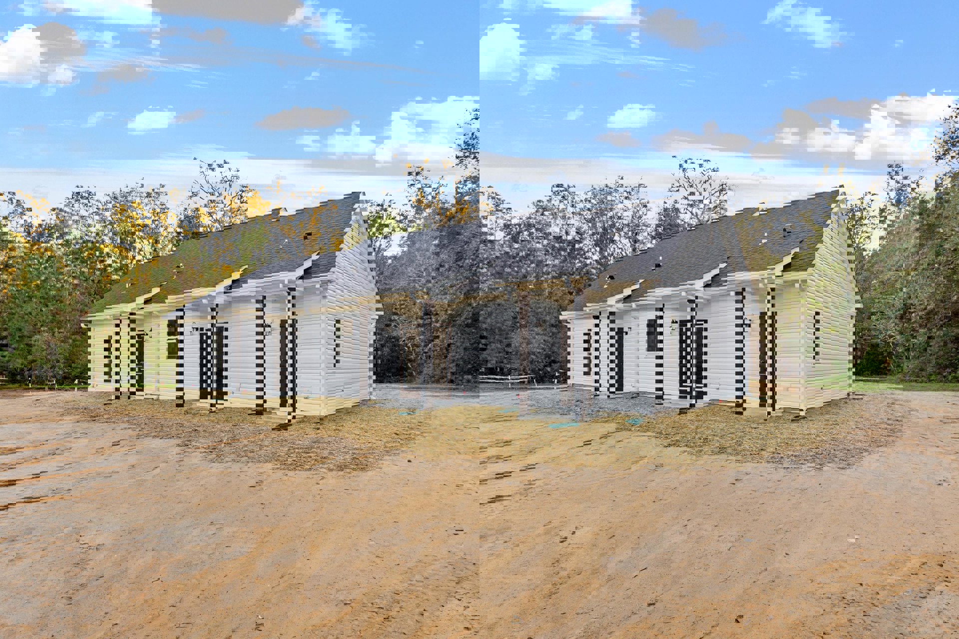 White house with black roof and doors, surrounded by trees, set along a dirt road under a blue sky