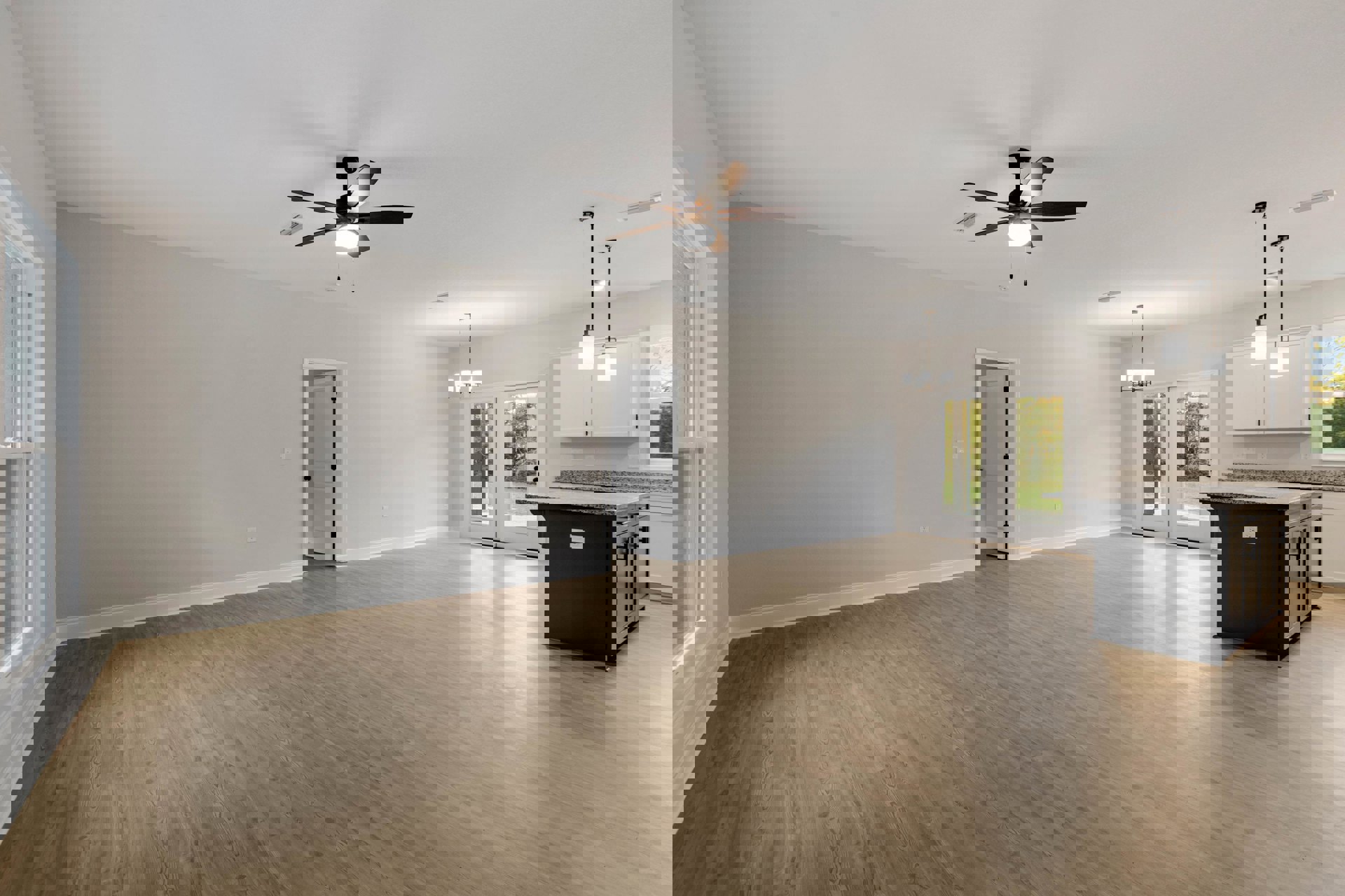 Open concept room featuring hardwood floors, white walls, a kitchen island with marble countertop, ceiling fan with light fixture, and a white door with black hardware