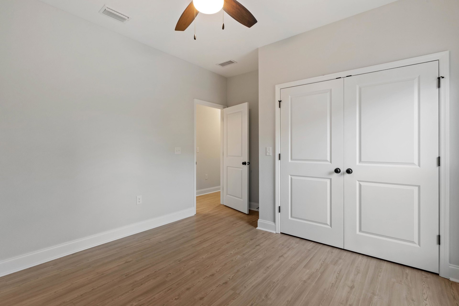 Wood floor with white walls, double white doors, ceiling fan, and light switch visible