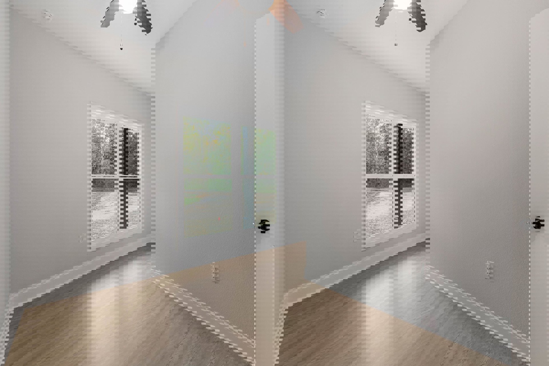 Wood flooring in a room with plaster walls, ceiling fan with light, and large window overlooking trees and forest.