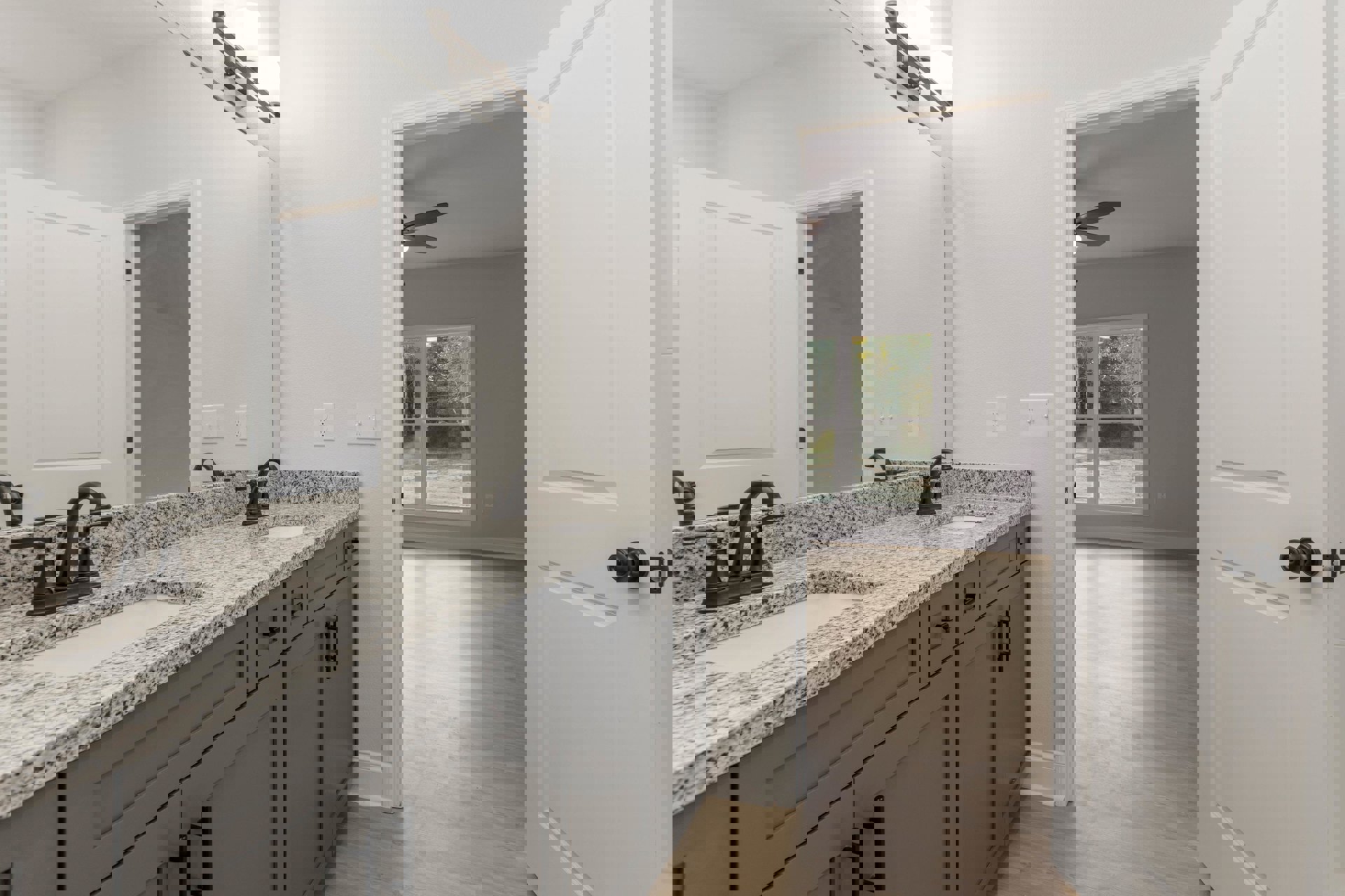 Bathroom with marble countertop, black-handled sink, white cabinetry, door with silver knob, window showing outdoor view, and modern light fixture.