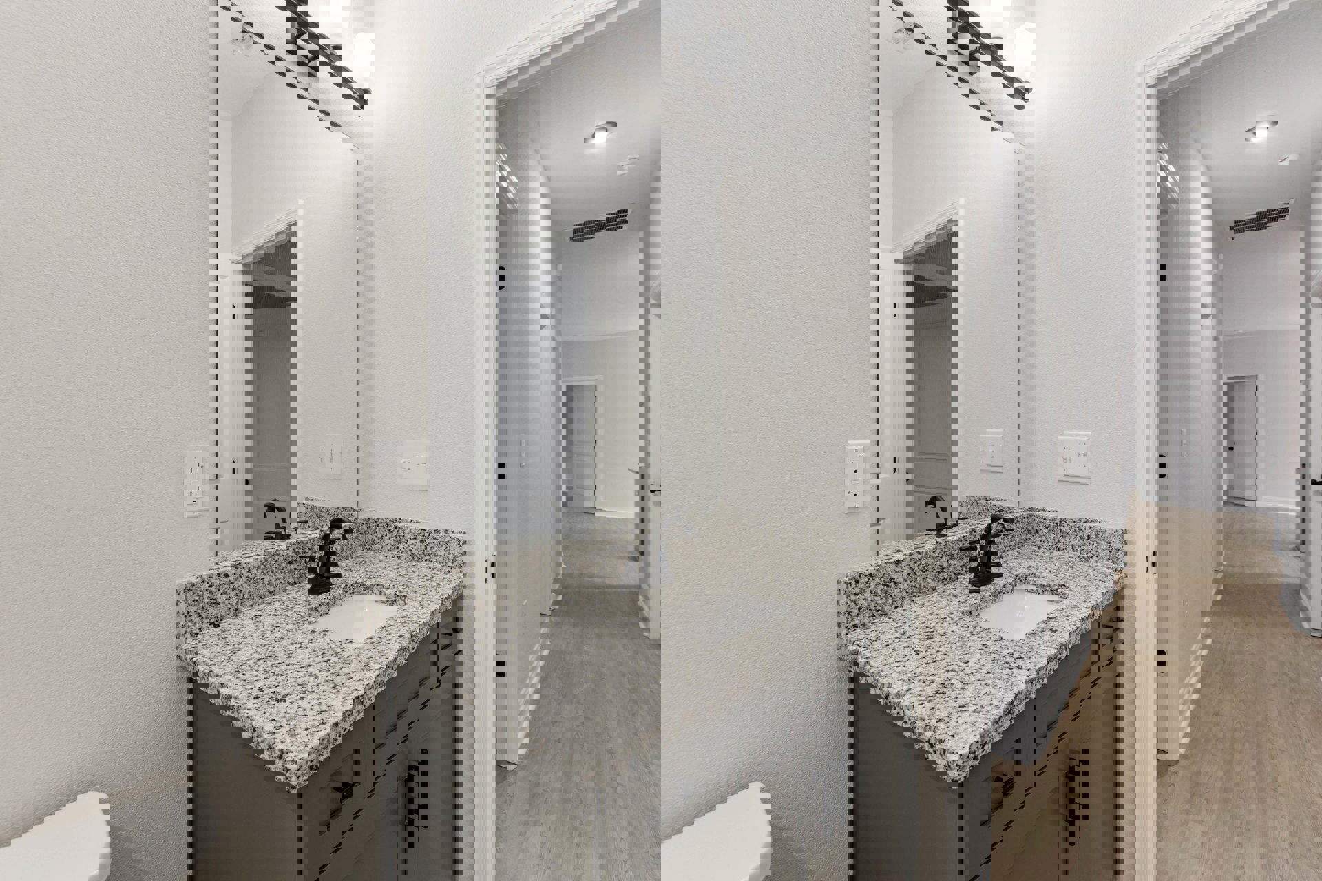 White bathroom vanity with black speckled countertop, undermount sink, chrome faucet, large wall mirror, white cabinetry with black knobs, and light tile flooring