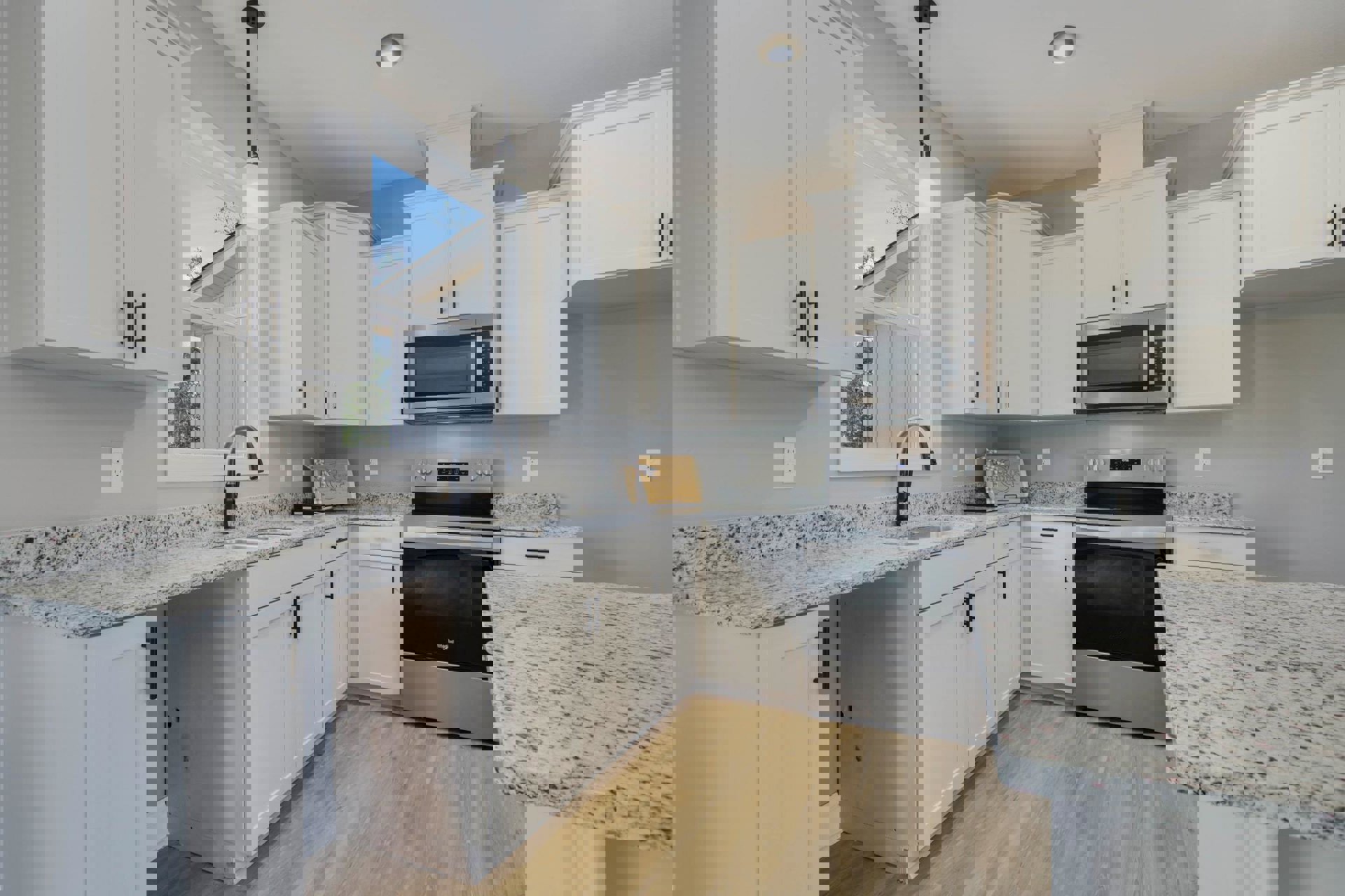 White kitchen cabinets, granite countertops, open microwave door, ceiling light, white wall outlet, close-up of granite surface