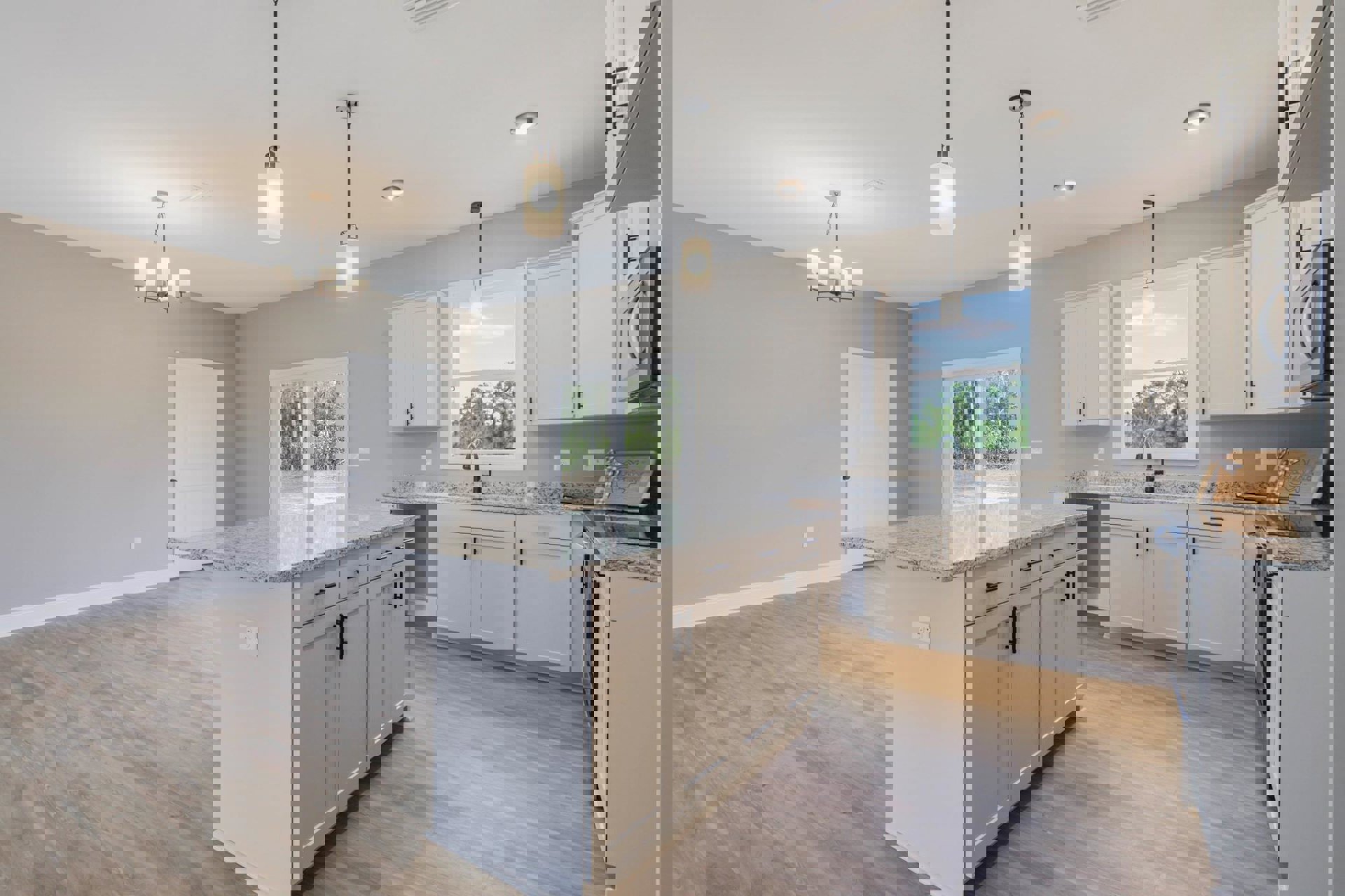 Spacious kitchen featuring a large granite island, wood flooring, white cabinetry, stainless steel appliances, sliding glass door, and windows with views of trees outside