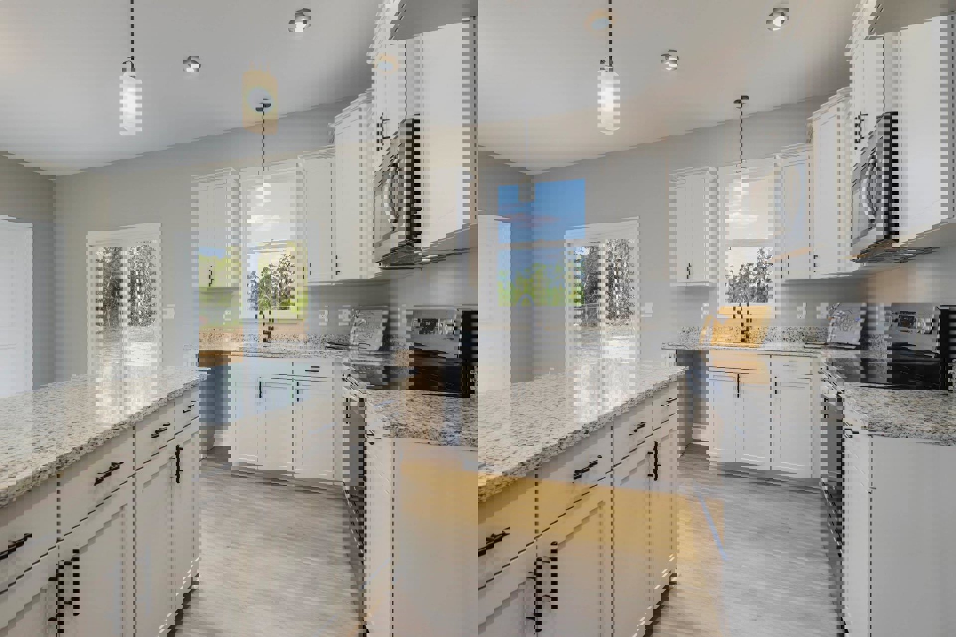 White kitchen with granite countertops, stainless steel stove and microwave, upper and lower cabinets, ceiling light, window providing natural light.