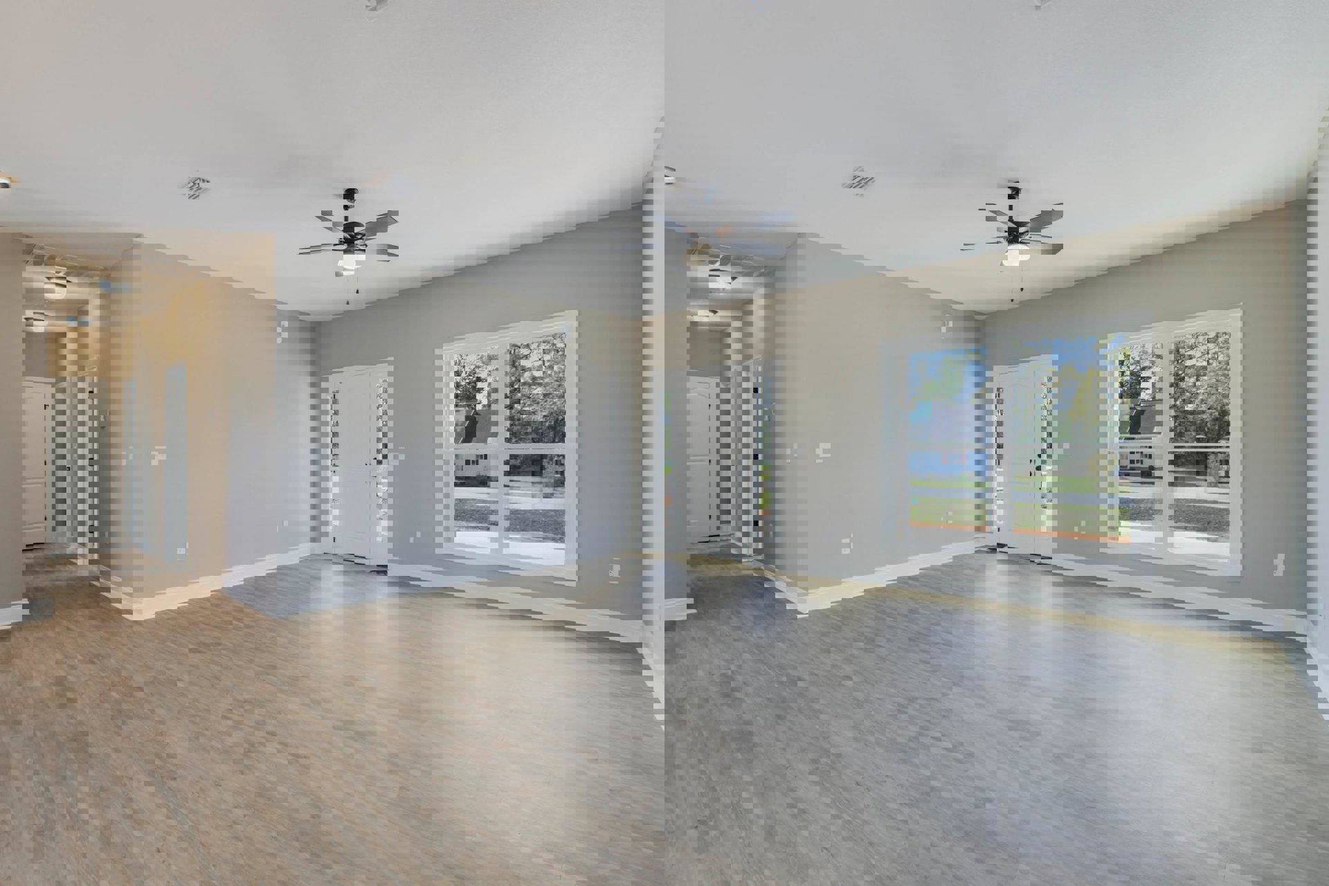 Room with wood flooring, white walls, ceiling fan with light, white door featuring black handle and knobs, windows offering view of neighboring house