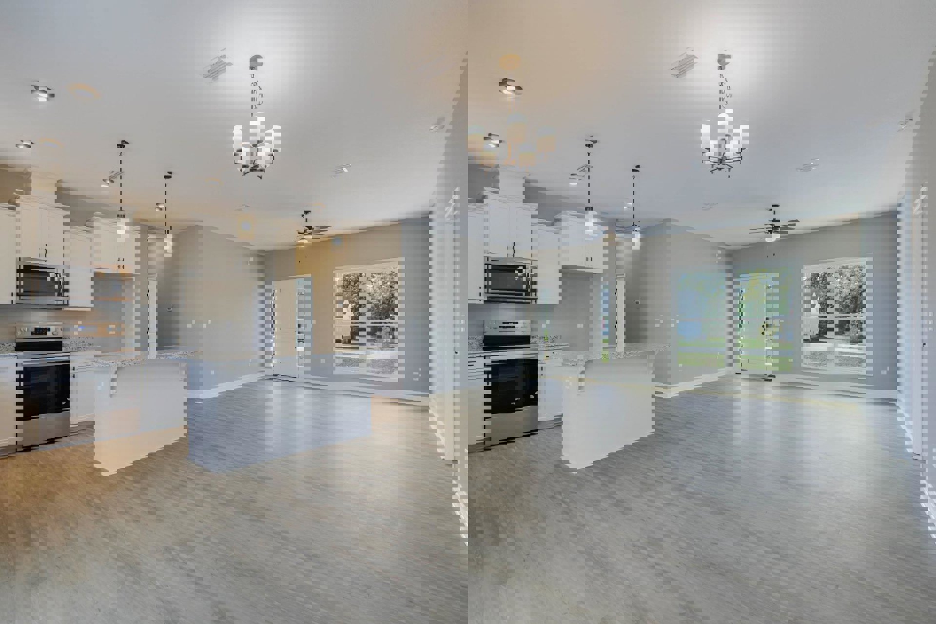 Spacious open-concept kitchen featuring a central island with marble countertop, wood flooring, white cabinetry, stainless steel stove, built-in microwave, and a window overlooking