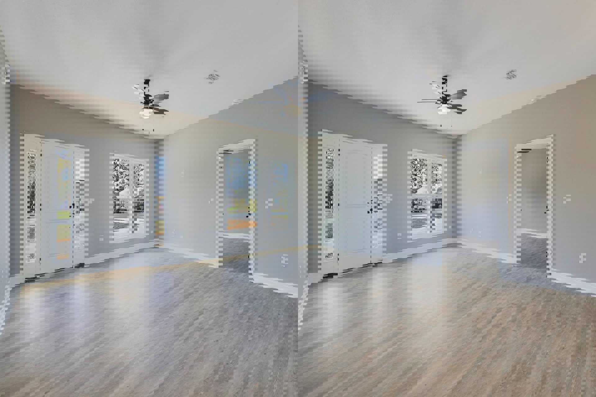 White room with wood flooring, ceiling fan with light, open white door featuring glass windows, plaster walls, and view of exterior house through window.