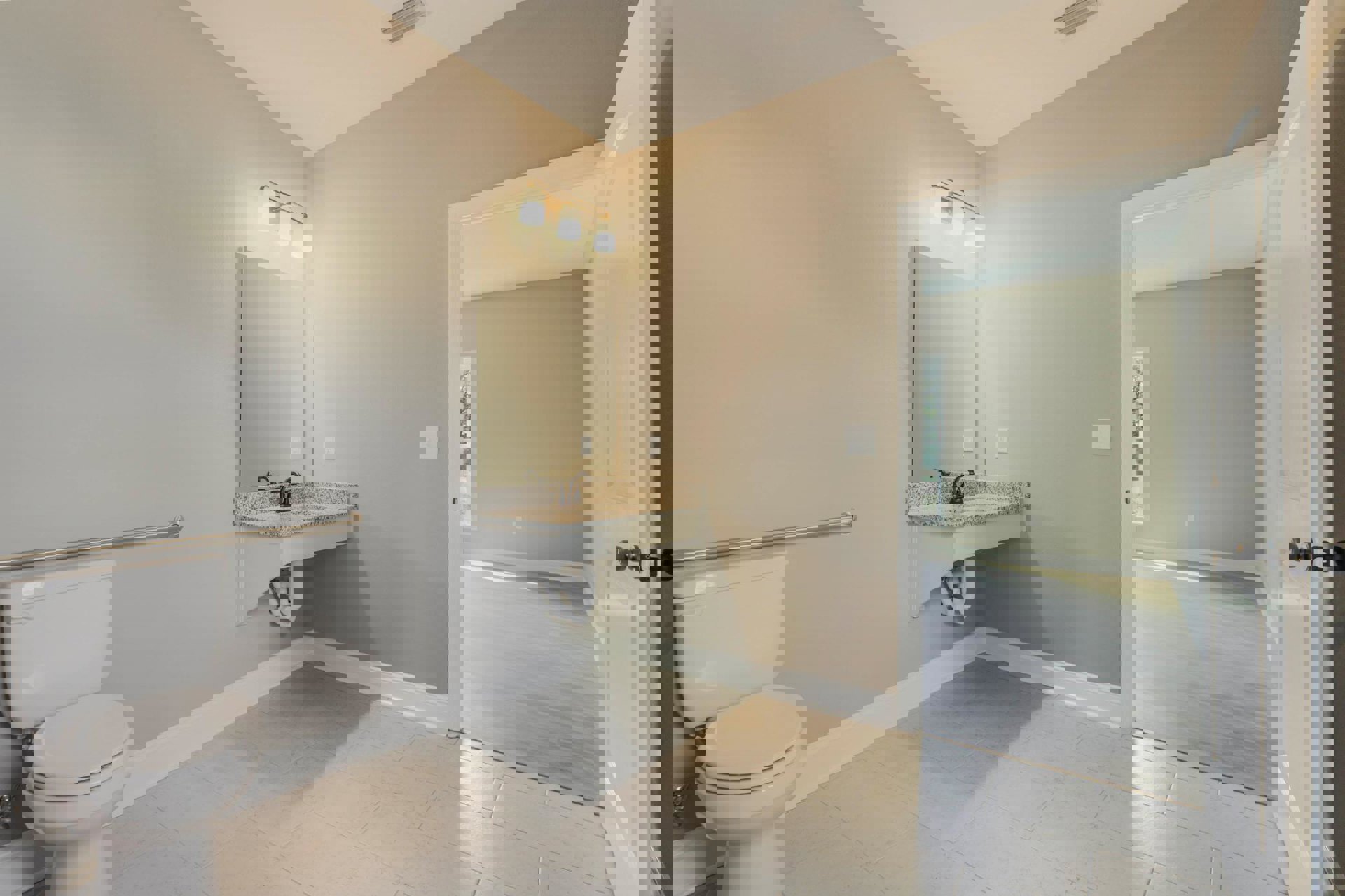 Bathroom with white tile floor, pedestal sink with exposed pipes, wall-mounted mirror, three-light fixture above, and closed white toilet.