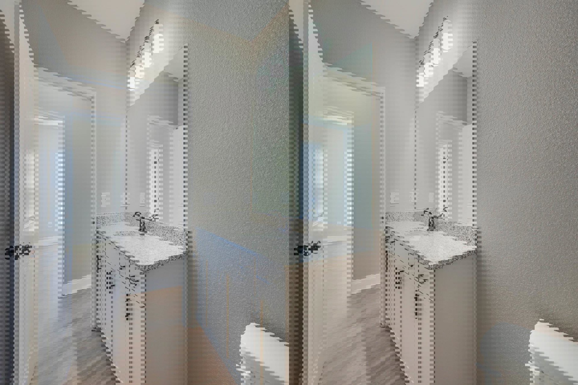 Modern bathroom featuring a rectangular mirror above a white sink with chrome faucet, light gray tile backsplash, white cabinetry, and a black-accented light fixture mounted on a