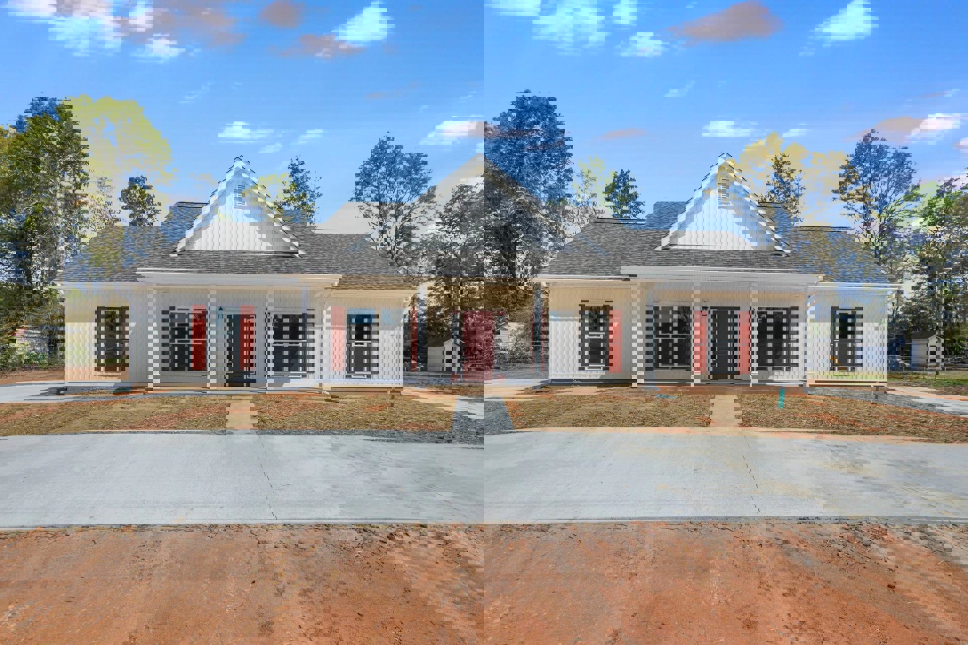 White siding house with red shutters, red front door with glass panels, white-framed windows, and landscaped front yard.