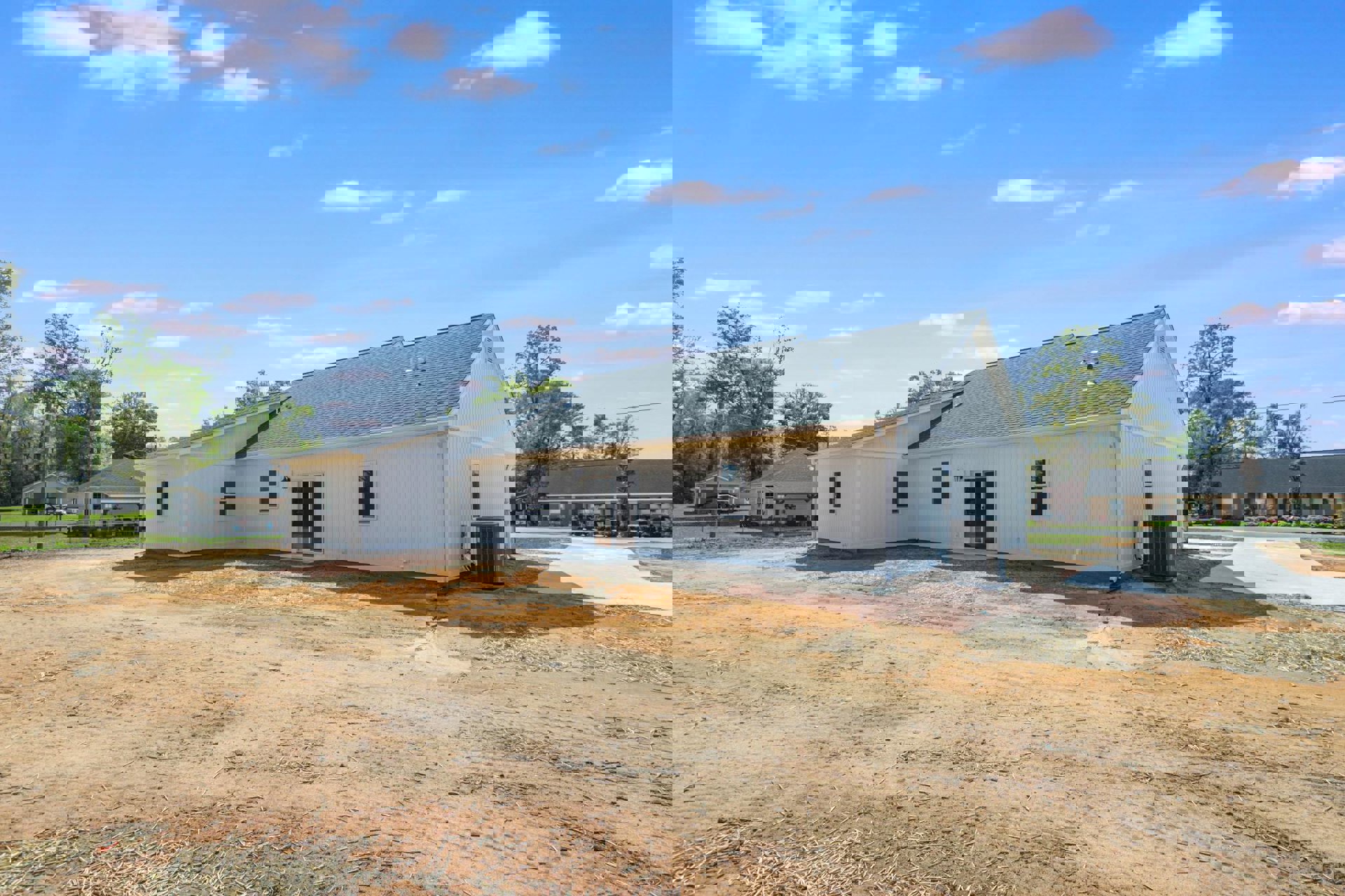 White house with glass door and white walls, surrounded by trees, dirt road in foreground, blue sky above