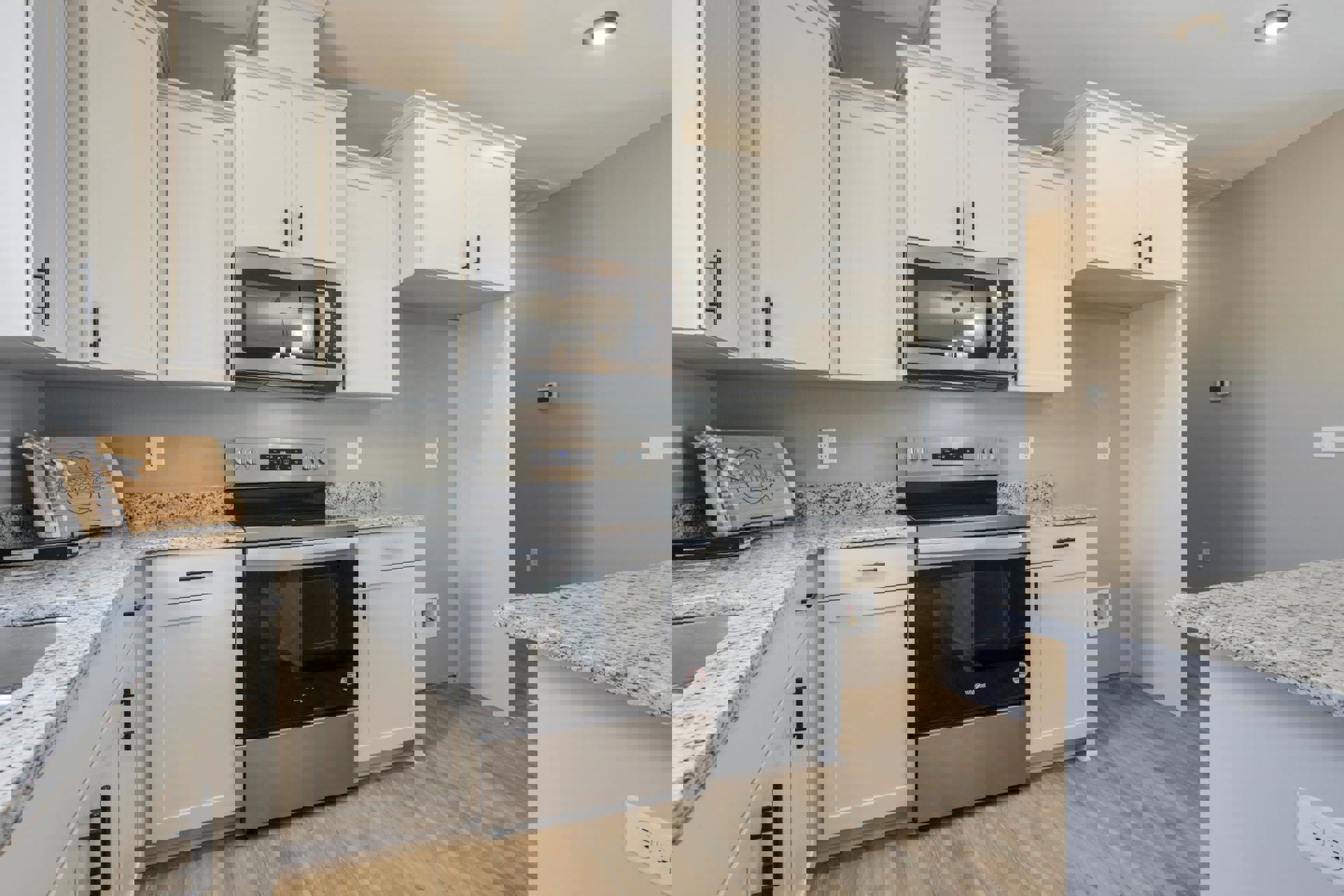 White shaker cabinets, black freestanding stove with matching microwave above, light quartz countertops, wooden cutting board with ribbon, recessed ceiling light, white paneled