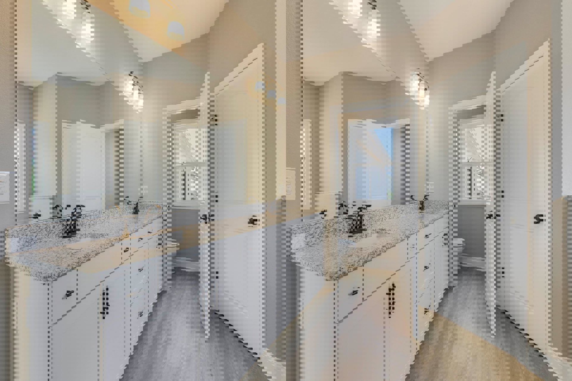 Bathroom with marble countertop, wood flooring, white cabinetry with black handles, white door with black knobs, window with white frame, and toilet.