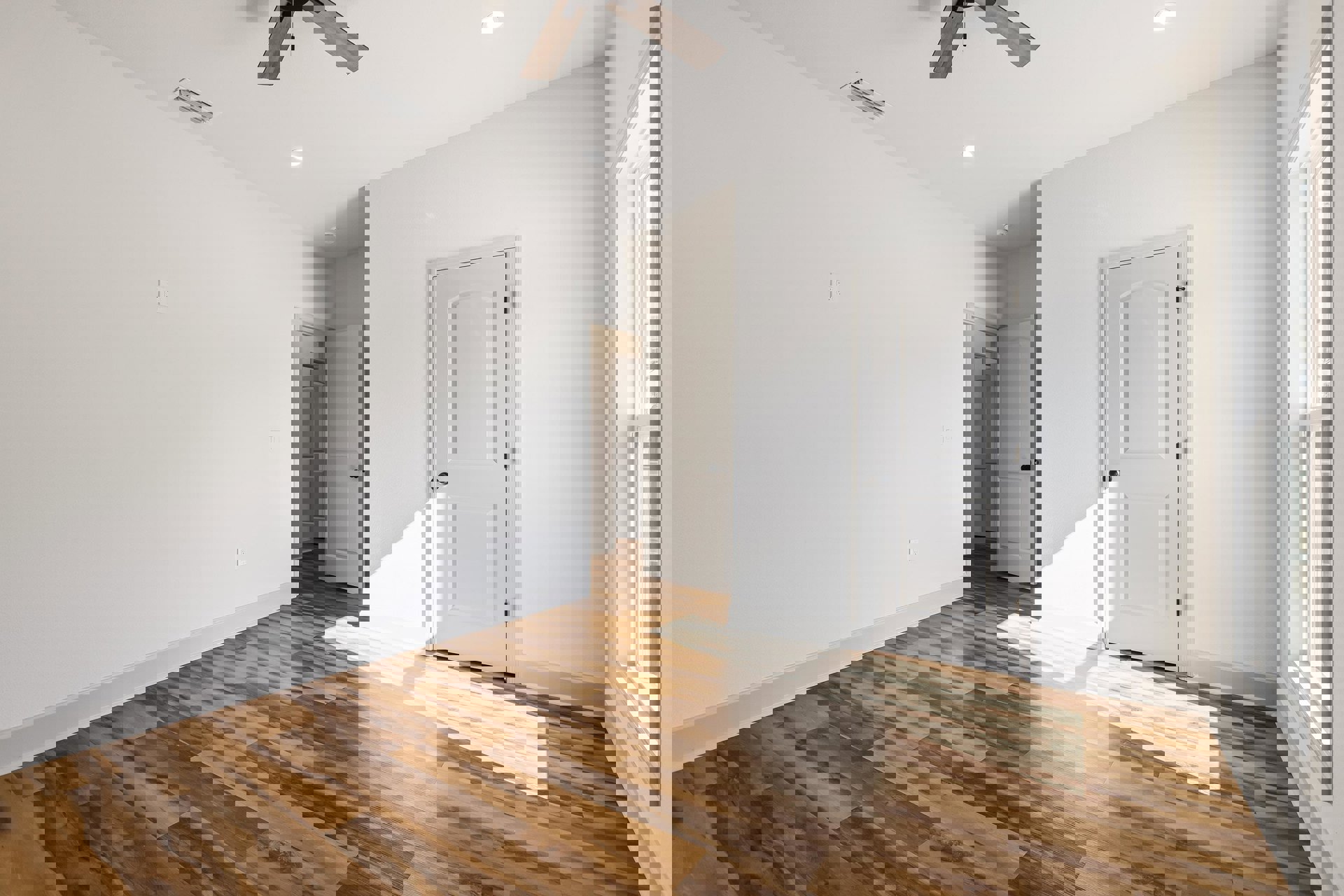 White walls, wood floor, white door with black knob, ceiling fan with light fixture, window with white frame