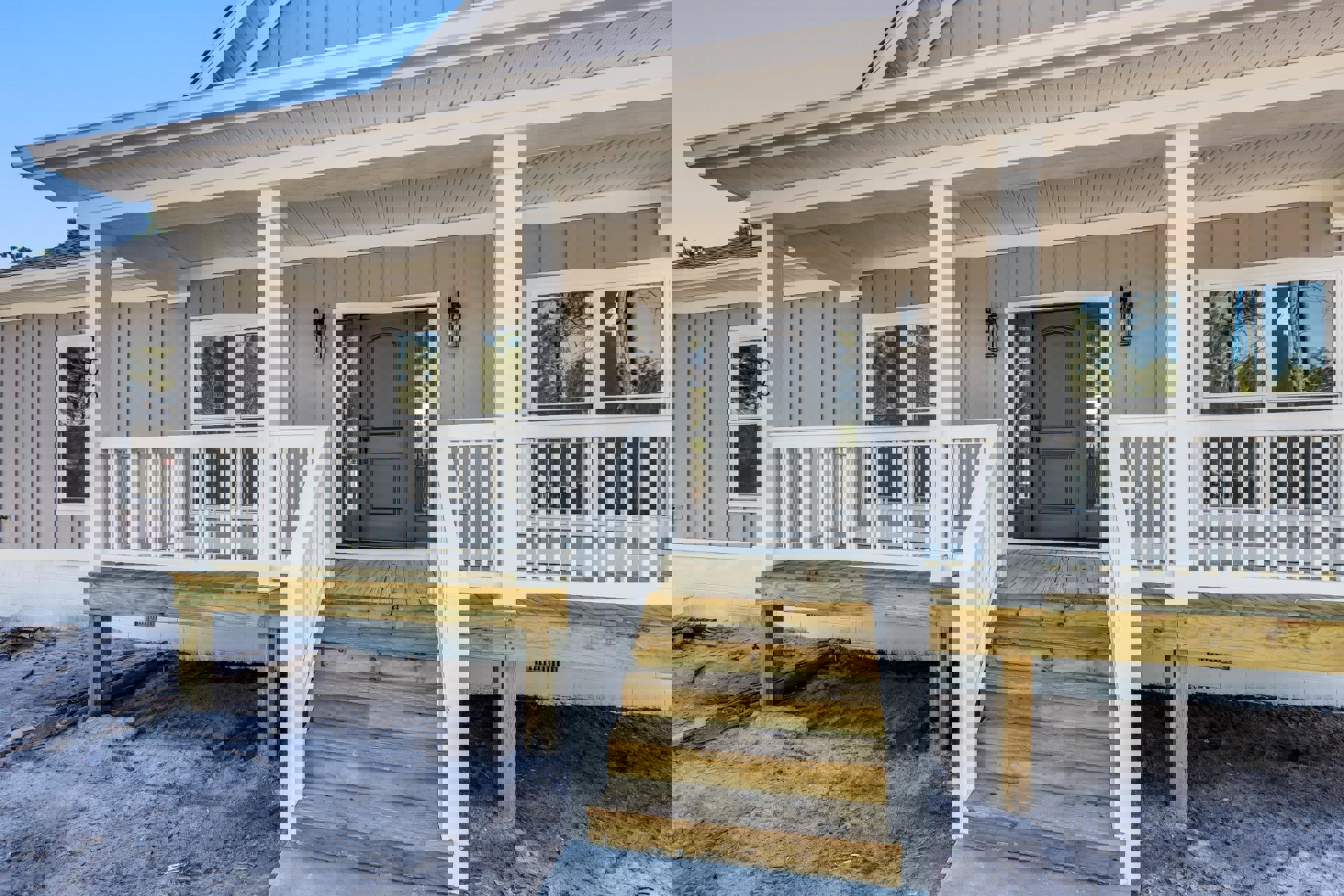 White siding house with wooden porch stairs, grey glass-paneled front door, white porch railing, and tree visible beside window