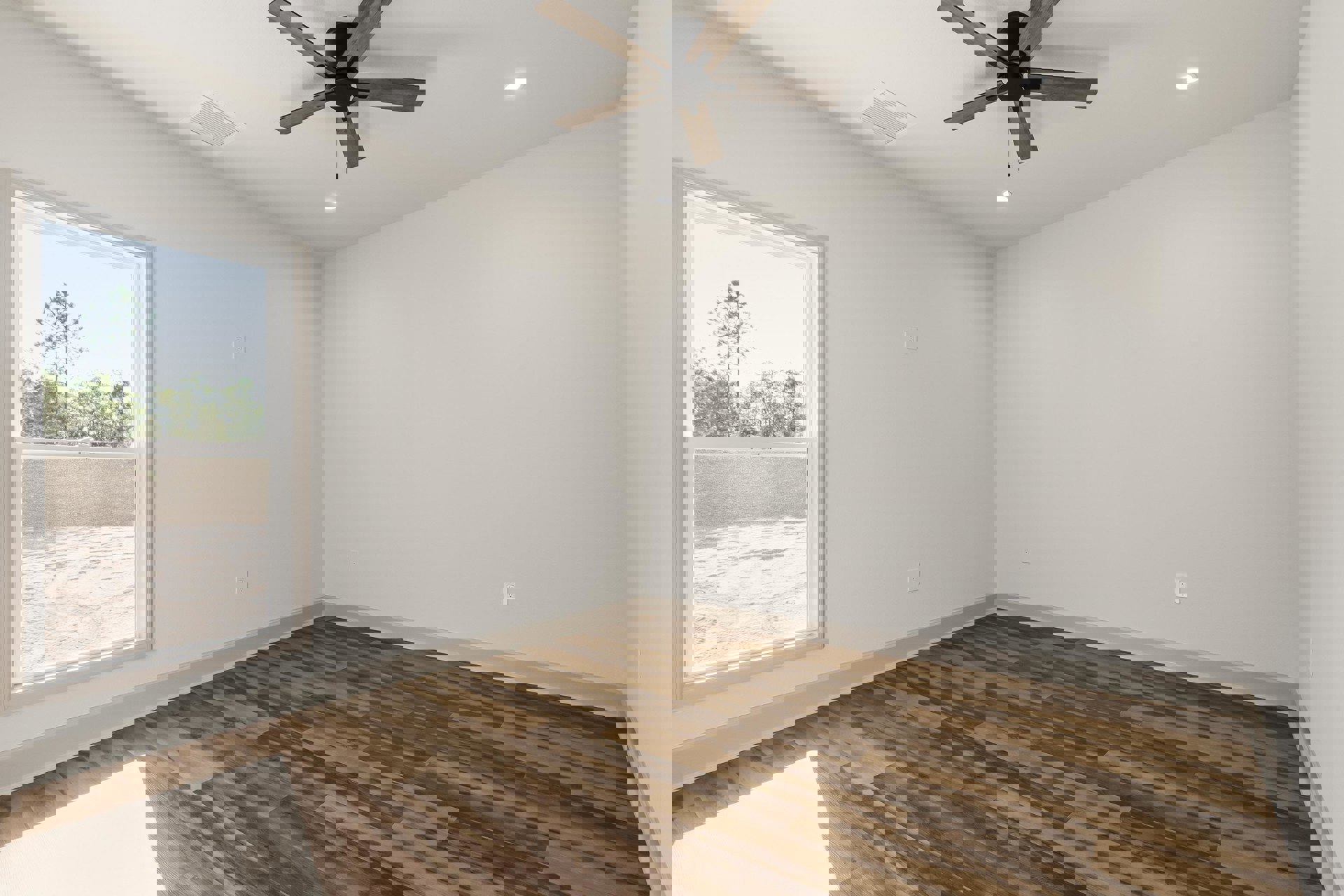 Ceiling fan with wood blades and light fixture above hardwood floor, white plaster walls, large window overlooking sandy beach and trees