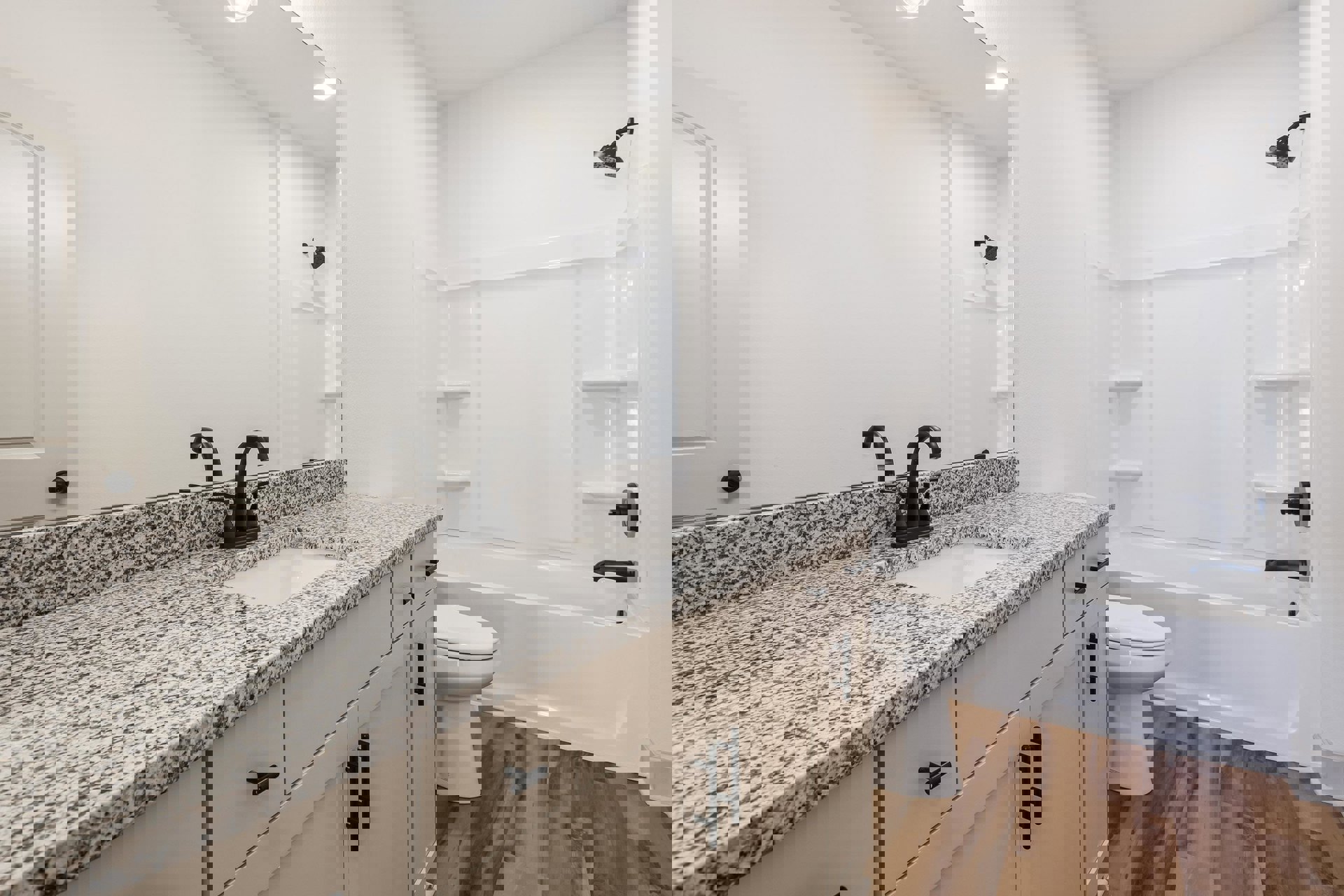 Bathroom with marble countertop, undermount sink and chrome faucet, white toilet with seat down, black shower head and matching vertical bar, white tile walls and cabinetry