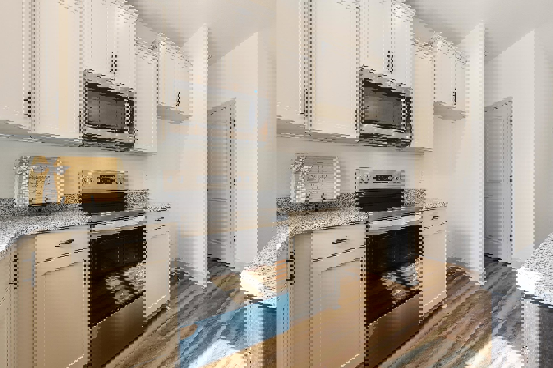 White kitchen cabinets paired with black appliances, including a microwave and stove, wood cutting board on the countertop, white door with black handle, and smooth counter