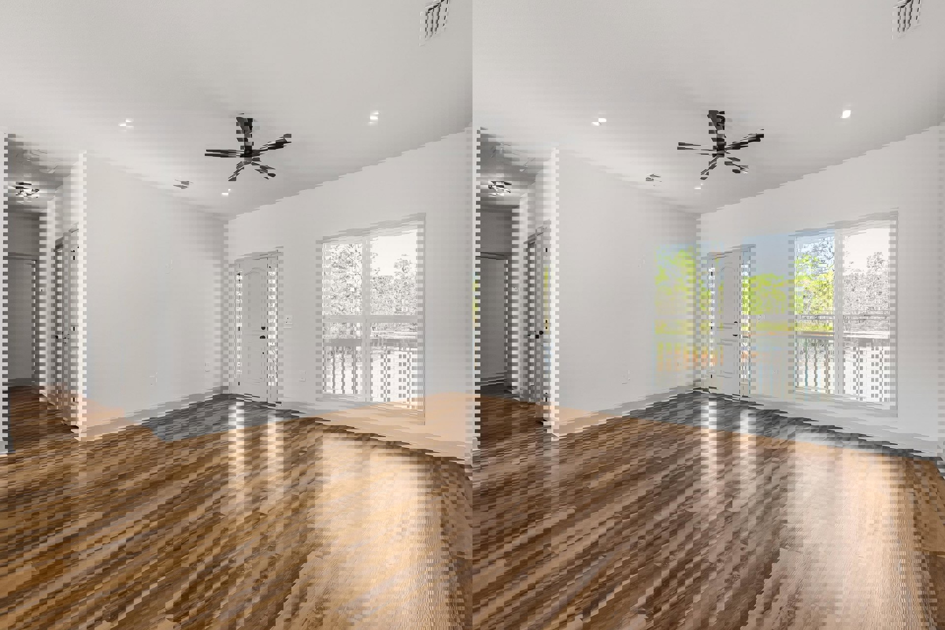 Wood flooring, white walls, ceiling fan with light, large window showing green trees, white doors with glass panels, rectangular thermostat with black border on wall