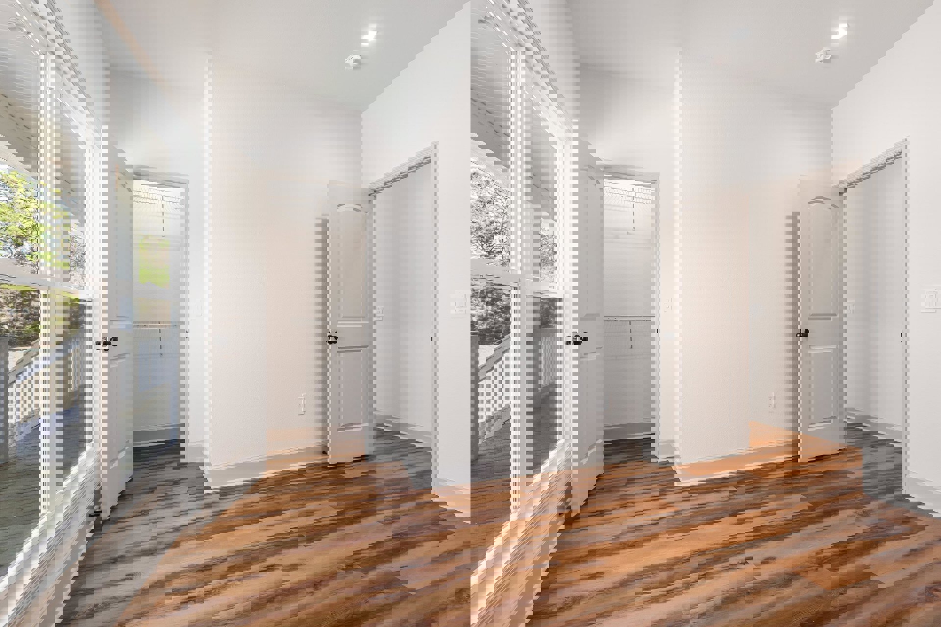 White walls, wood flooring, white door with black handle, window with white frame, metal bar mounted on wall