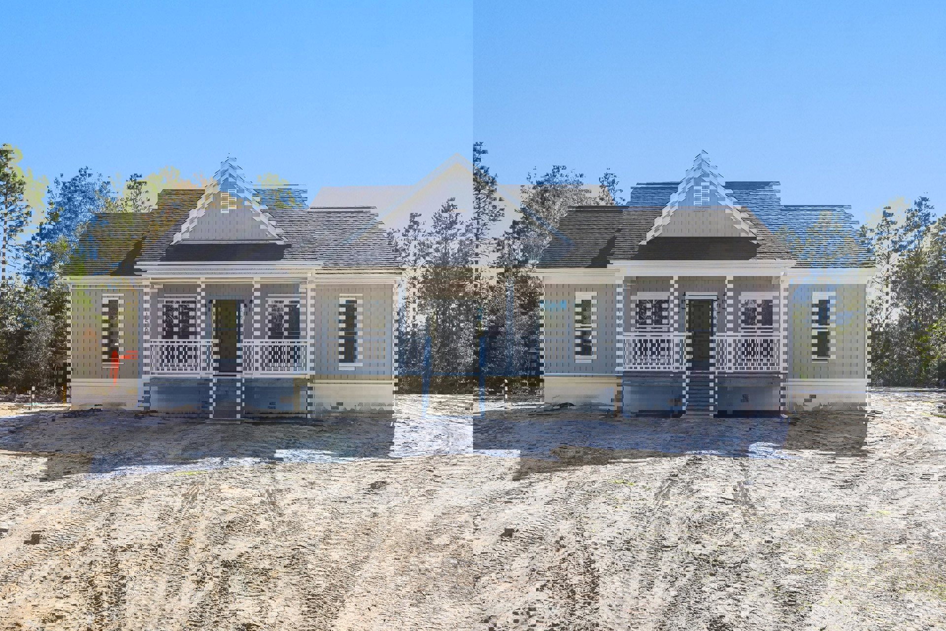 White house with black glass-paneled door, white-framed windows including one with broken glass, covered porch, dirt road with tire tracks, trees in background