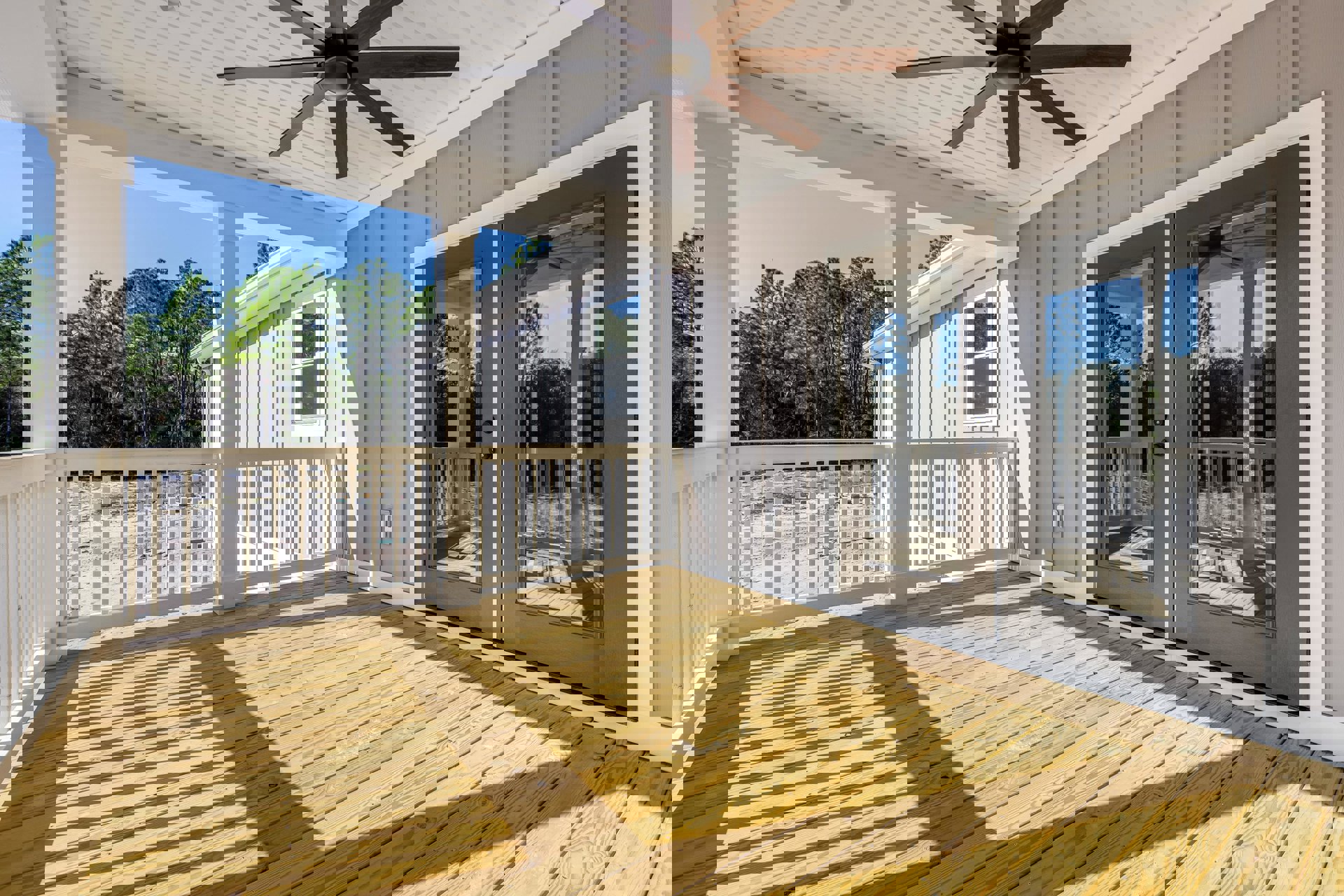 Wood deck porch with white railing, ceiling fan featuring wood blades and light fixture, white-framed window overlooking trees