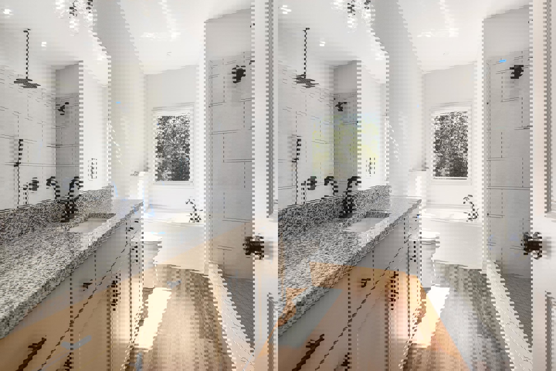 Modern bathroom with freestanding white bathtub, rectangular sink on white countertop, ceiling-mounted shower head, closed white toilet, large window overlooking trees, and