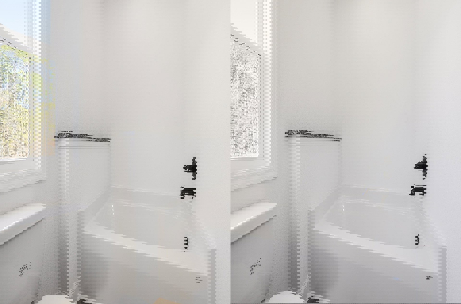 White tiled bathroom with freestanding bathtub, modern toilet, chrome faucet, and large window overlooking leafy trees