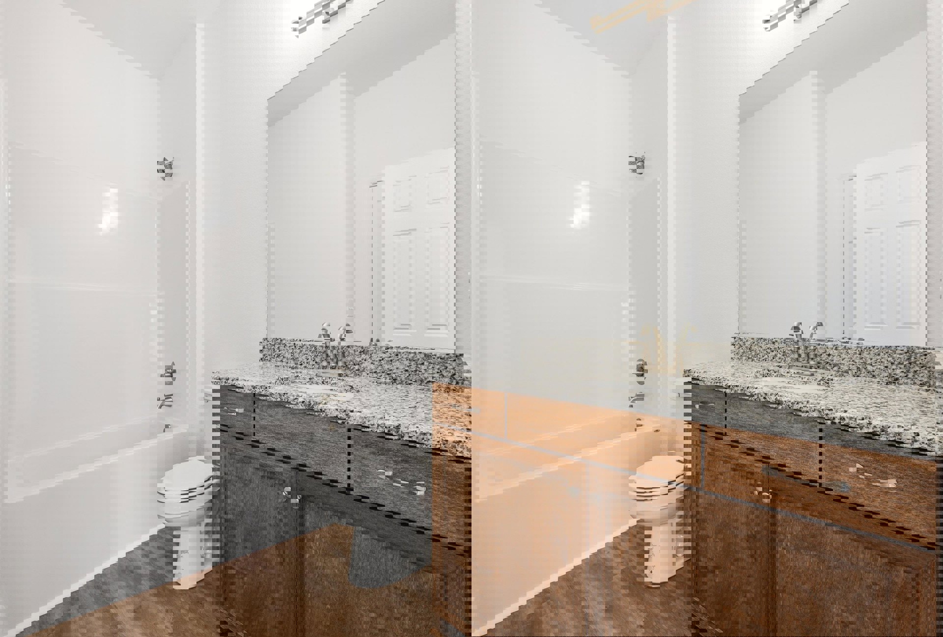 Modern bathroom featuring white toilet with closed lid, rectangular sink set in light wood cabinetry, chrome faucet, tiled walls, and partial view of white bathtub.