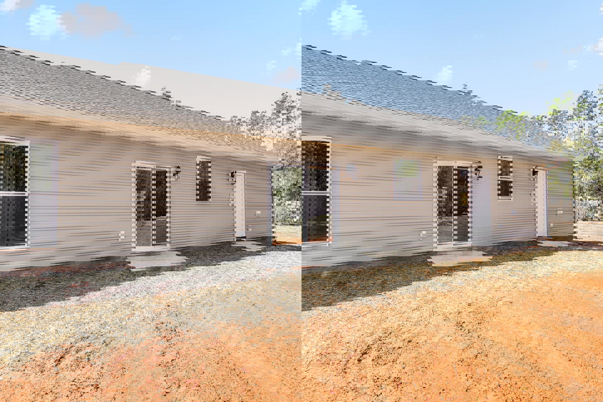 Modern home exterior with glass door reflecting trees, gravel driveway, white-framed window, light siding, and small patio area