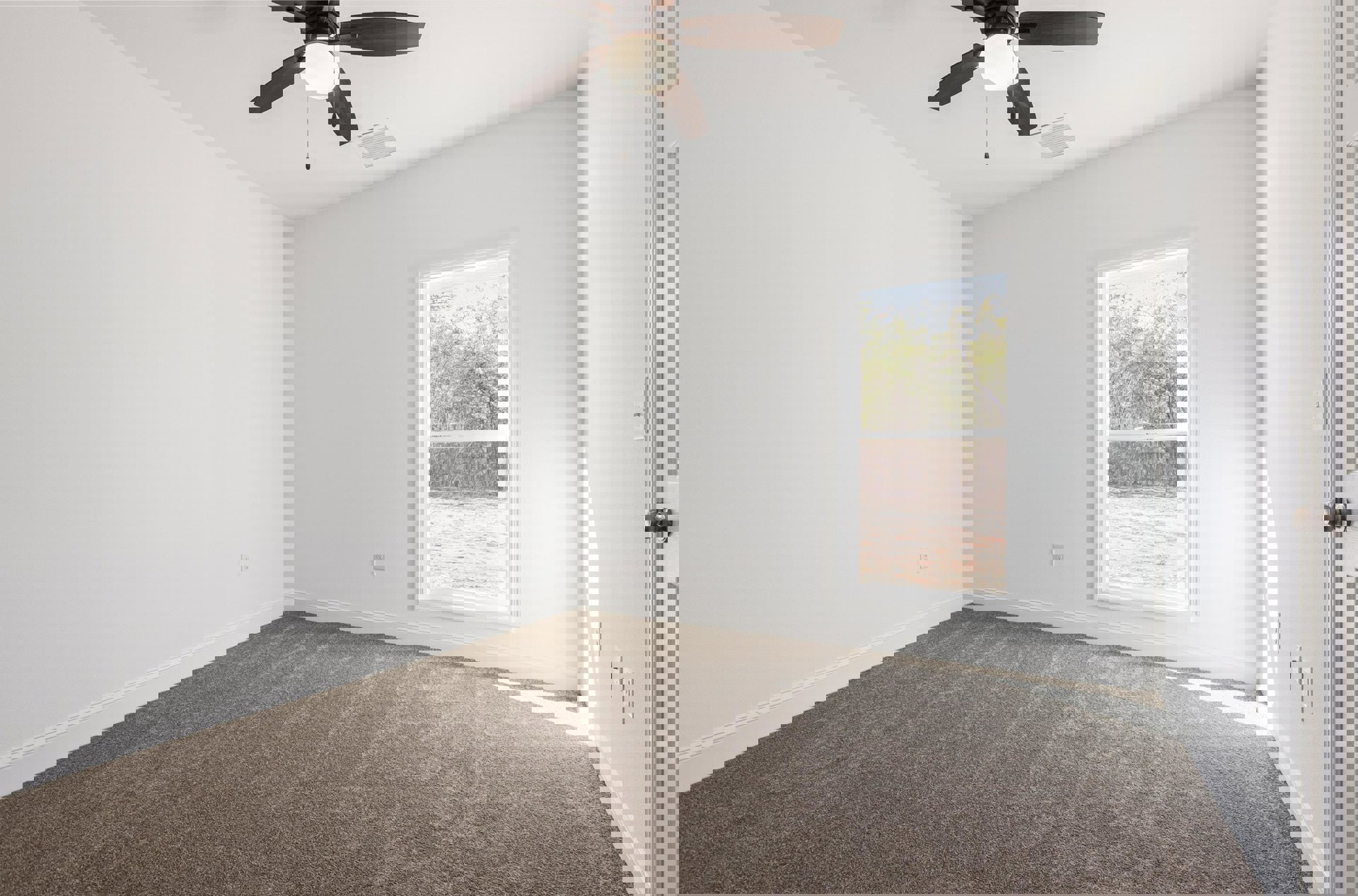 Carpeted room with a ceiling fan and light, single window showing trees outside, white walls, and baseboard trim.