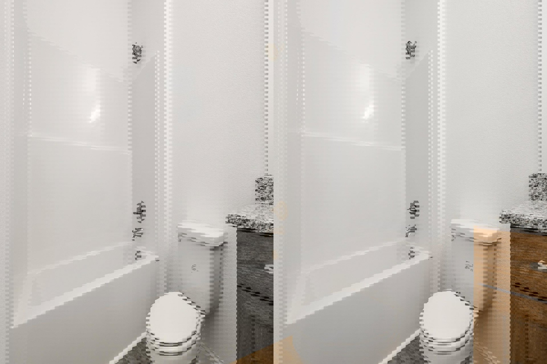 White bathroom with glossy tile walls, white toilet with lid up, built-in bathtub, chrome showerhead, and metal faucet knob