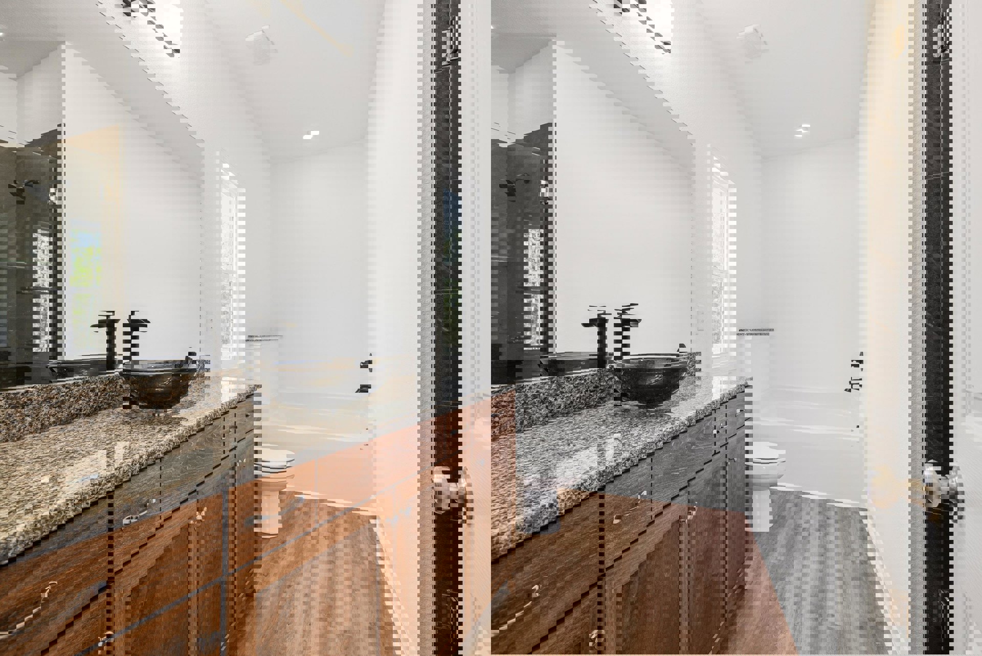 Bathroom with marble countertop vanity, undermount sink, freestanding bathtub, white toilet, tiled walls, chrome shower head, and modern cabinetry