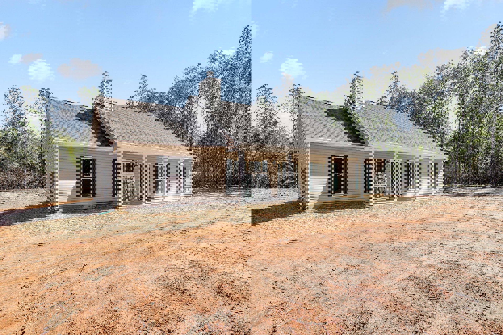 Two-story house with white-framed windows, broken glass pane, brick chimney, shingle roof, and dirt yard under partly cloudy sky