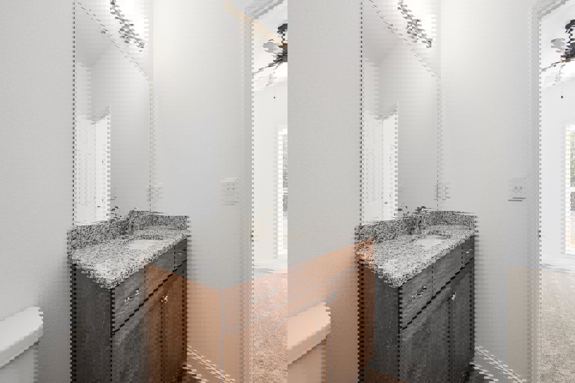 White bathroom with granite countertop, undermount sink, chrome faucet, large wall mirror, white cabinetry, and tiled walls