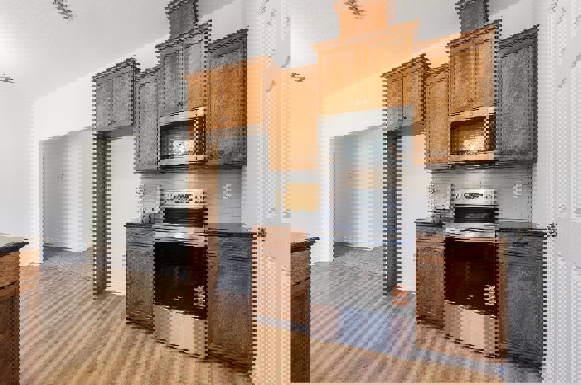 Kitchen with natural wood cabinets, stainless steel microwave oven above a glass-door stove, light stone countertops, and tile flooring