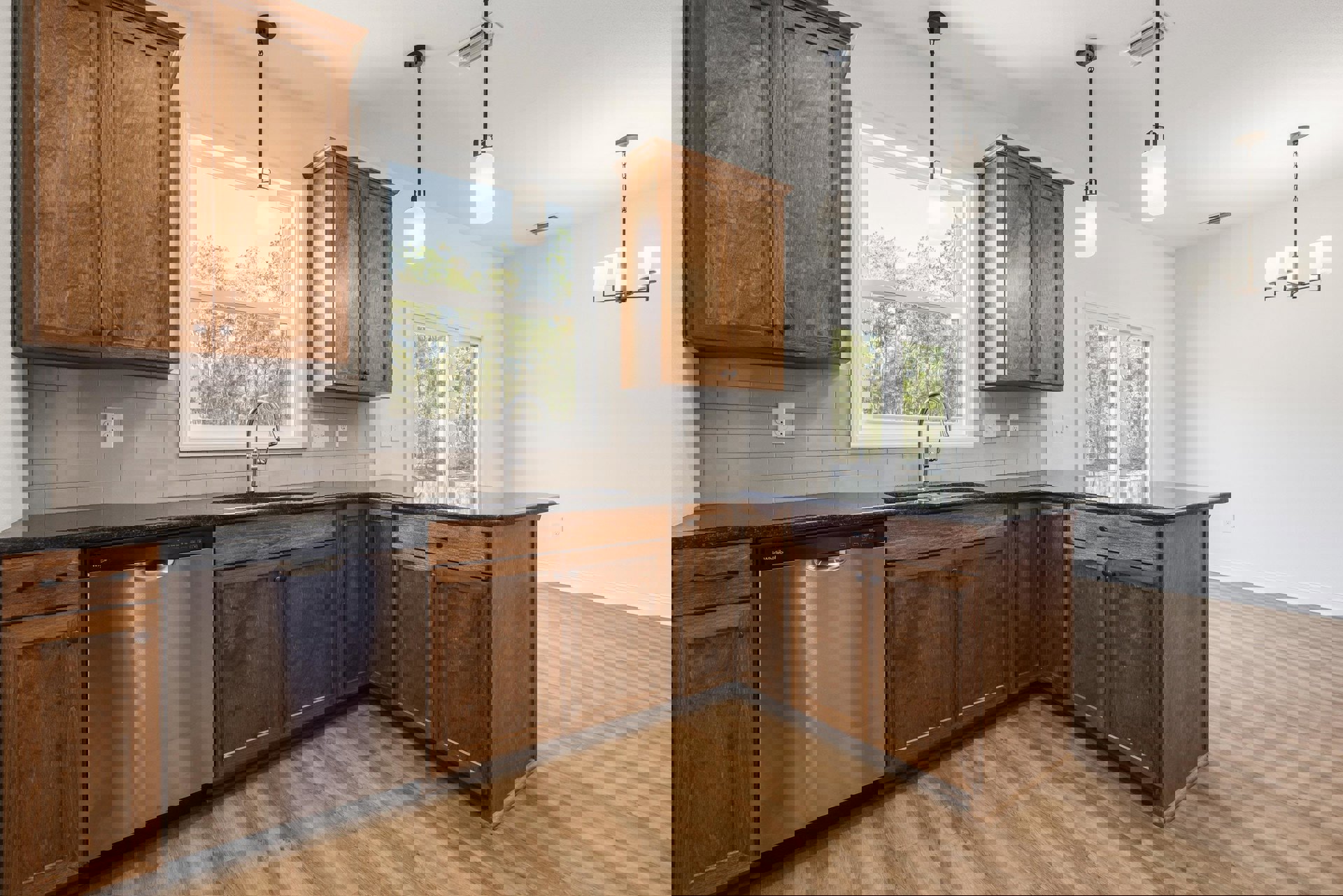 Wood cabinets with brushed metal handles, stainless steel dishwasher, white quartz countertop, overhead pendant light, window above sink, light hardwood flooring